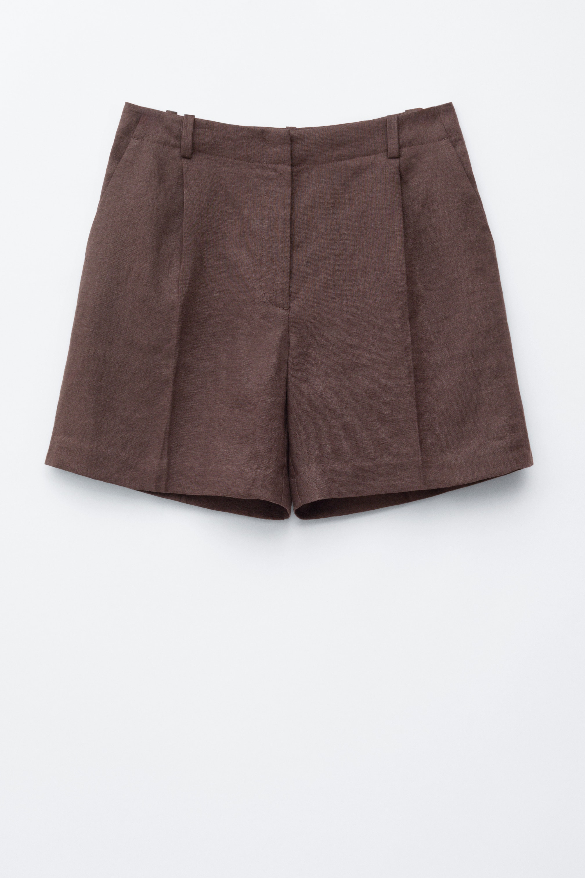 Ver imagen más grande: Los pantalones cortos de lino marrón se presentan de frente, con una cintura que incluye trabillas para cinturón y una bragueta con cremallera. Se aprecian dos pliegues frontales en cada pierna y bolsillos laterales inclinados.