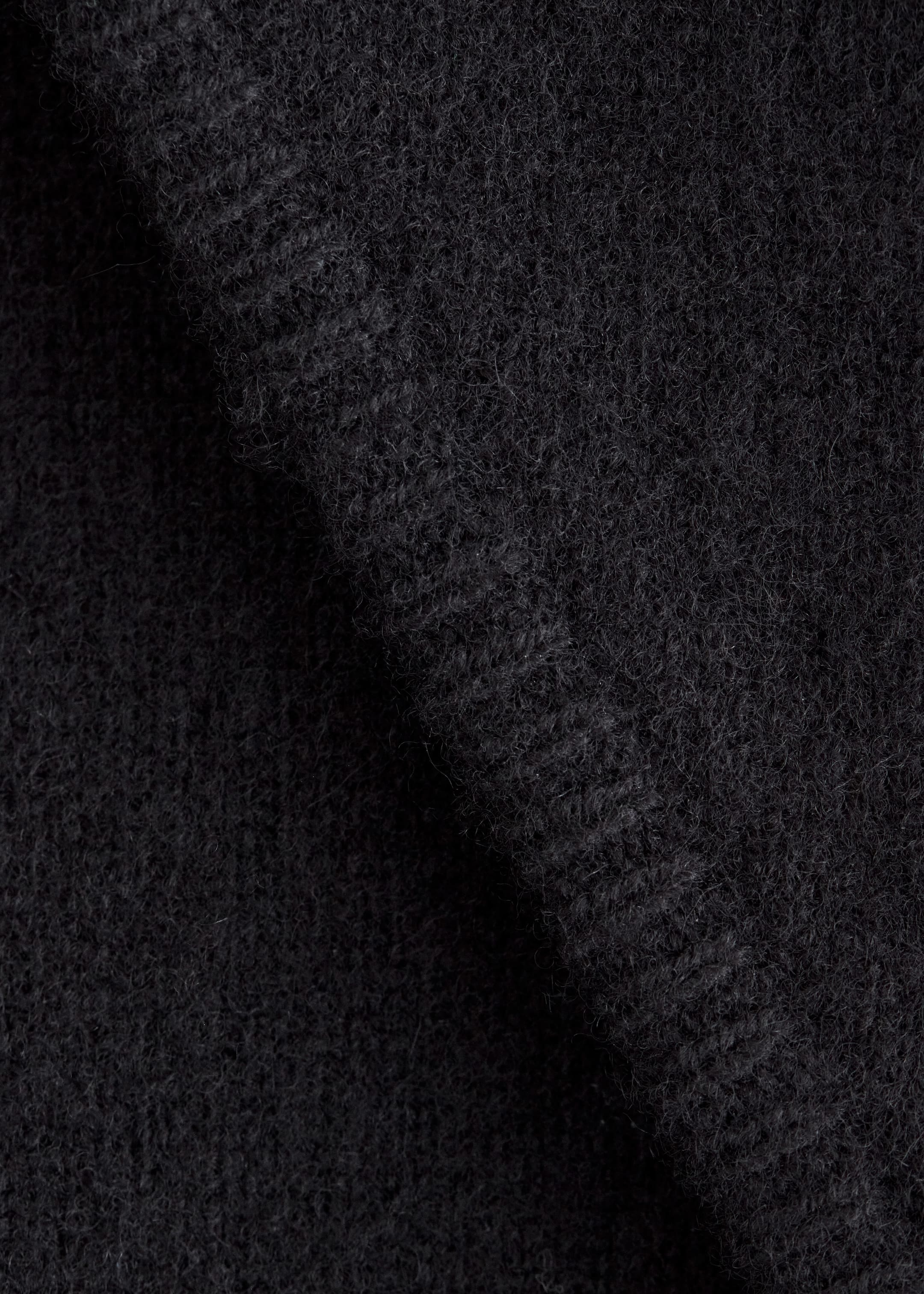 Visualizza immagine più grande: Un tessuto di lana scuro viene presentato in primo piano, mostrando una texture morbida, densa e lanuginosa con fibre visibili e pieghe naturali.