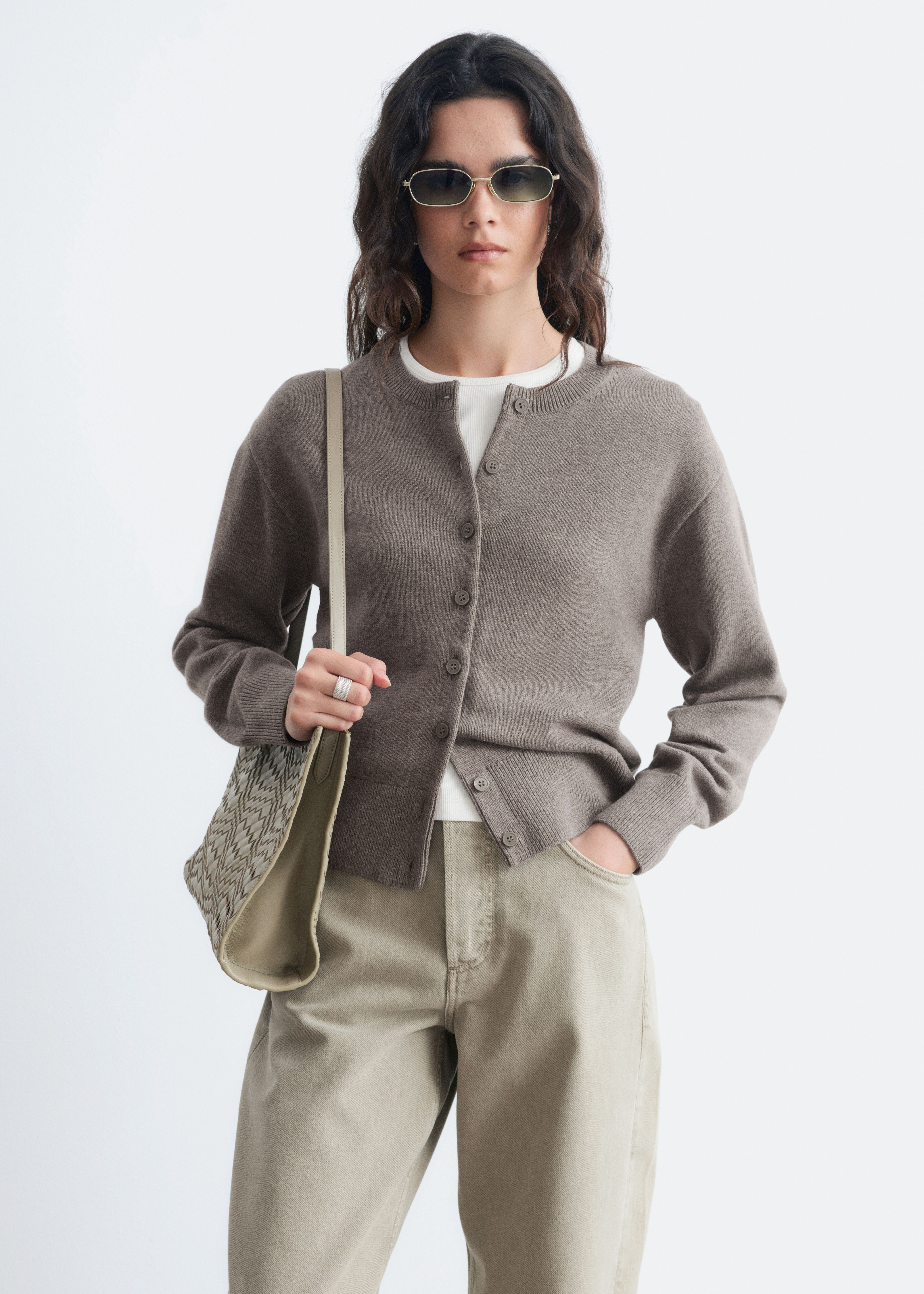 Eine braune Strickjacke wird von vorne präsentiert, mit einem runden Halsausschnitt und gerippten Details. Gerippte Bänder bilden auch die Bündchen und den Saum, und tonale Knöpfe verlaufen entlang der Vorderseite der Strickjacke.