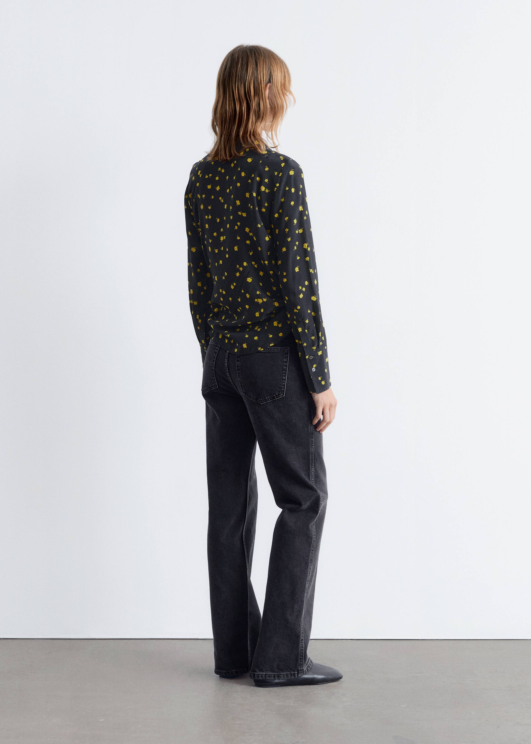 Ver imagem maior: Um top preto de manga comprida com pequenas formas amarelas dispersas está a ser usado, visto de costas e ligeiramente inclinado para a direita. Está a ser combinado com jeans pretos lavados de perna reta que mostram bolsos traseiros visíveis e costuras nas pernas.