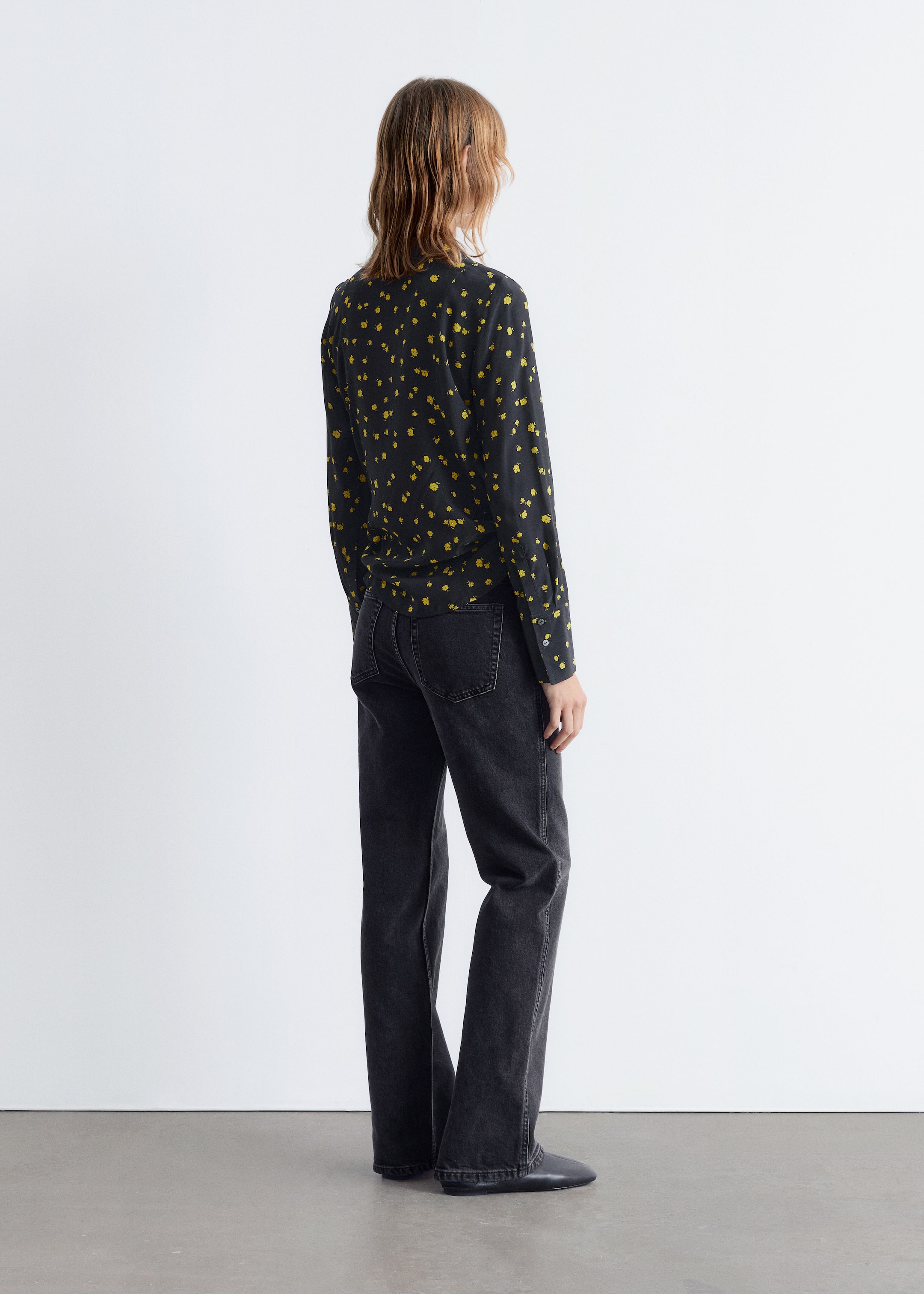 View larger image: A black long-sleeved top featuring small, scattered yellow shapes is being worn, seen from the back and angled slightly to the right. It is being paired with washed black, straight-leg jeans that are displaying visible back pockets and leg seams.