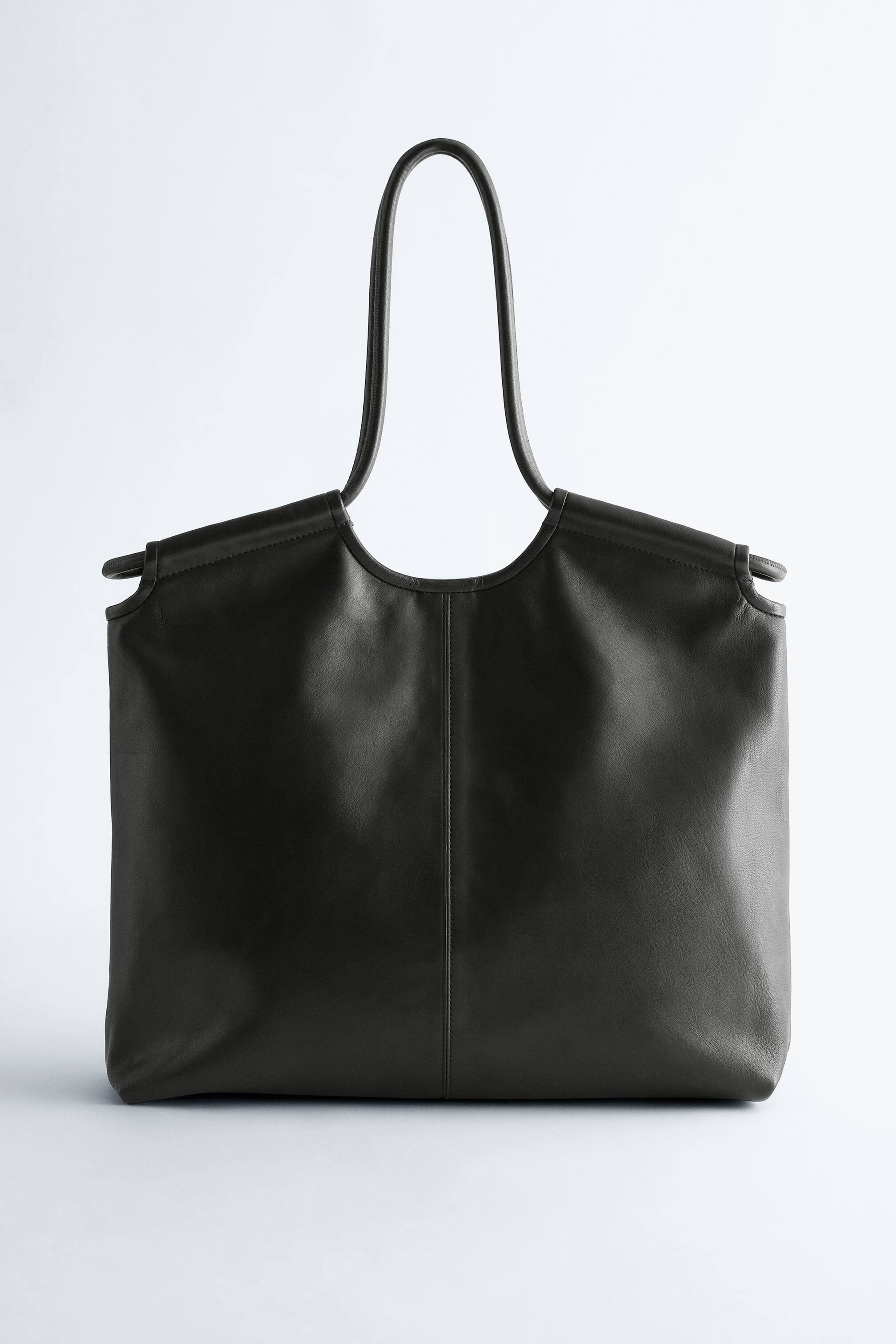 Visualizza l'immagine ingrandita: Una borsa in pelle grigio scuro viene presentata FRONTE, con un corpo rettangolare dai bordi morbidi. Due manici sottili e arcuati si alzano dal bordo superiore della borsa, incorniciando un'ampia apertura curva, e una cucitura verticale corre lungo il suo centro frontale.