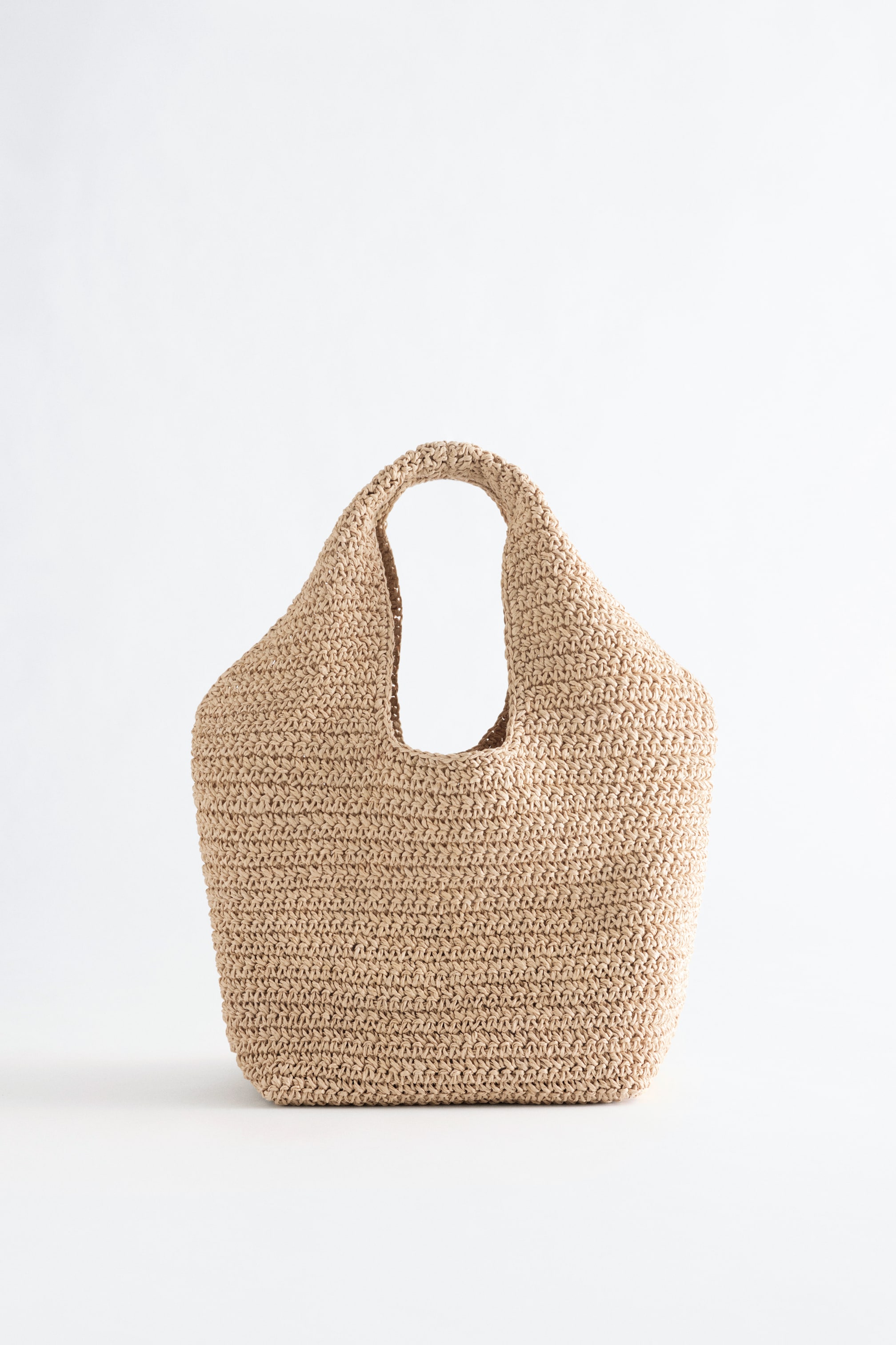 Agrandir l'image: Un sac cabas brun clair est debout et fait face à l'avant. Il présente un matériau en paille de papier tressé, créant une silhouette courbée avec des poignées supérieures intégrées.