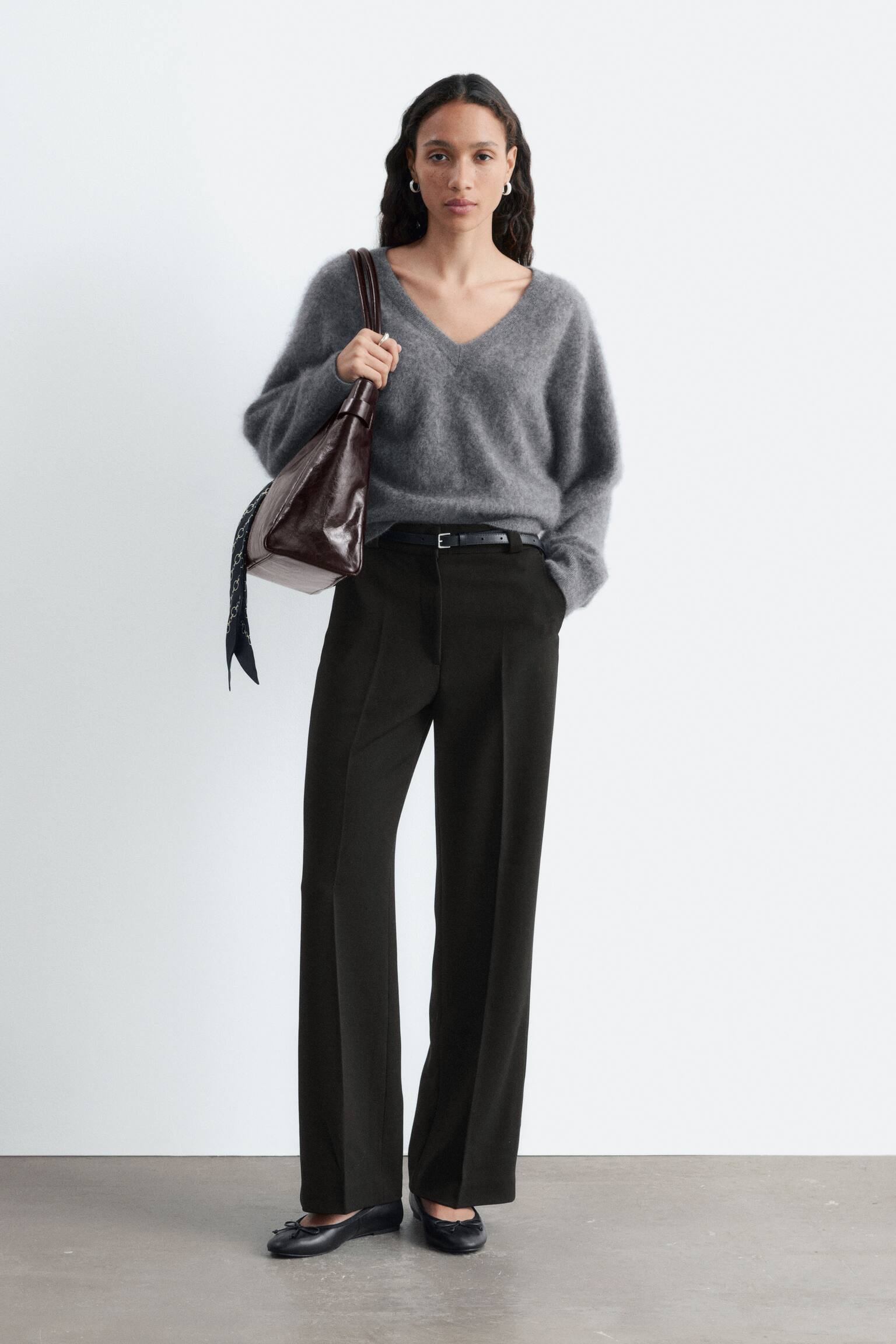 Un pantalon noir à jambes larges est exposé de face, avec des plis marqués et deux poches en biais. Le pantalon comprend également une fermeture éclair et des passants de ceinture. - 1