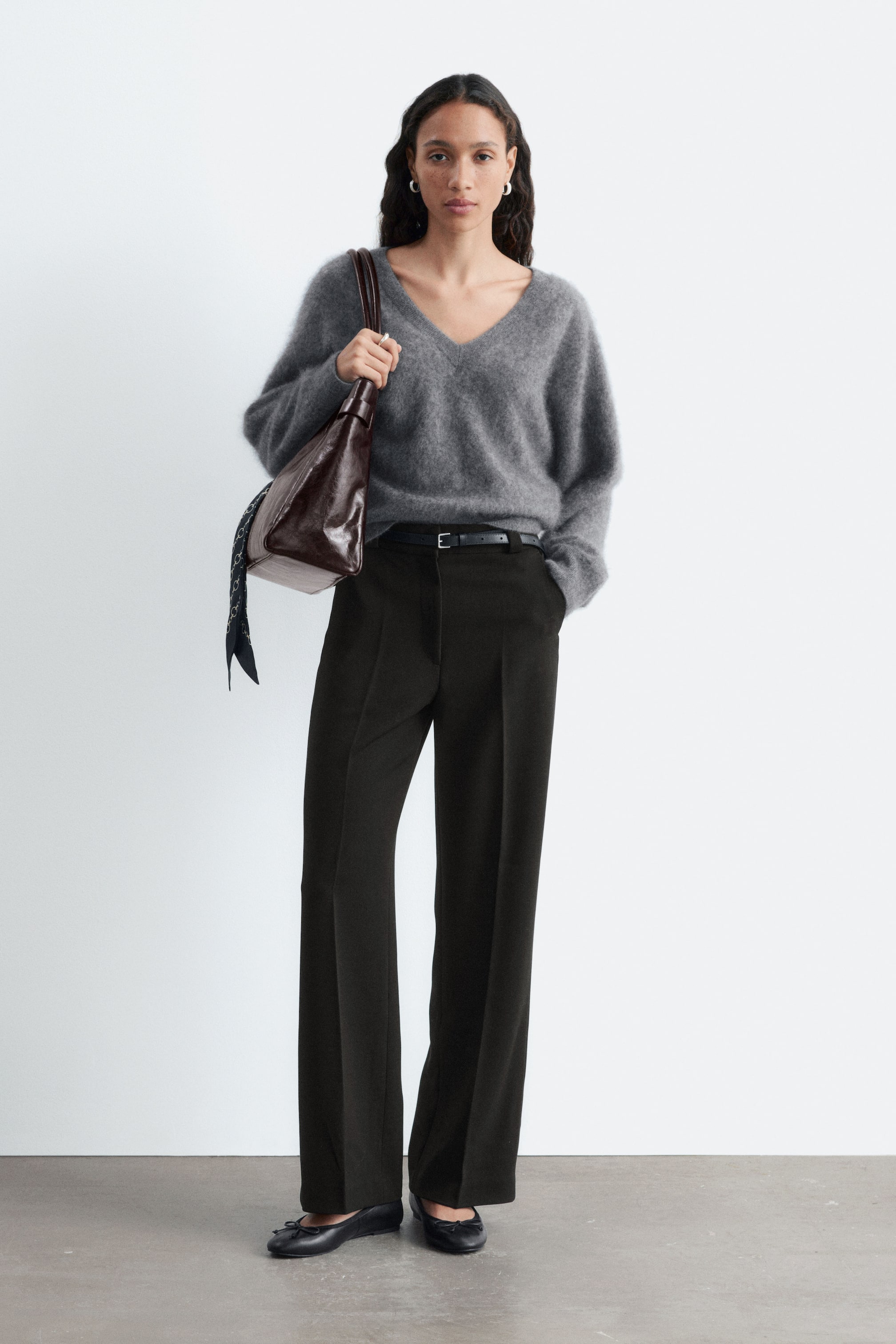 Visualizza l'immagine ingrandita: Pantaloni scuri con gamba lunga e dritta e pieghe stirate nette sono indossati dalla modella. La modella sta infilando la mano nella tasca laterale, e una cintura è allacciata in vita ai pantaloni.
