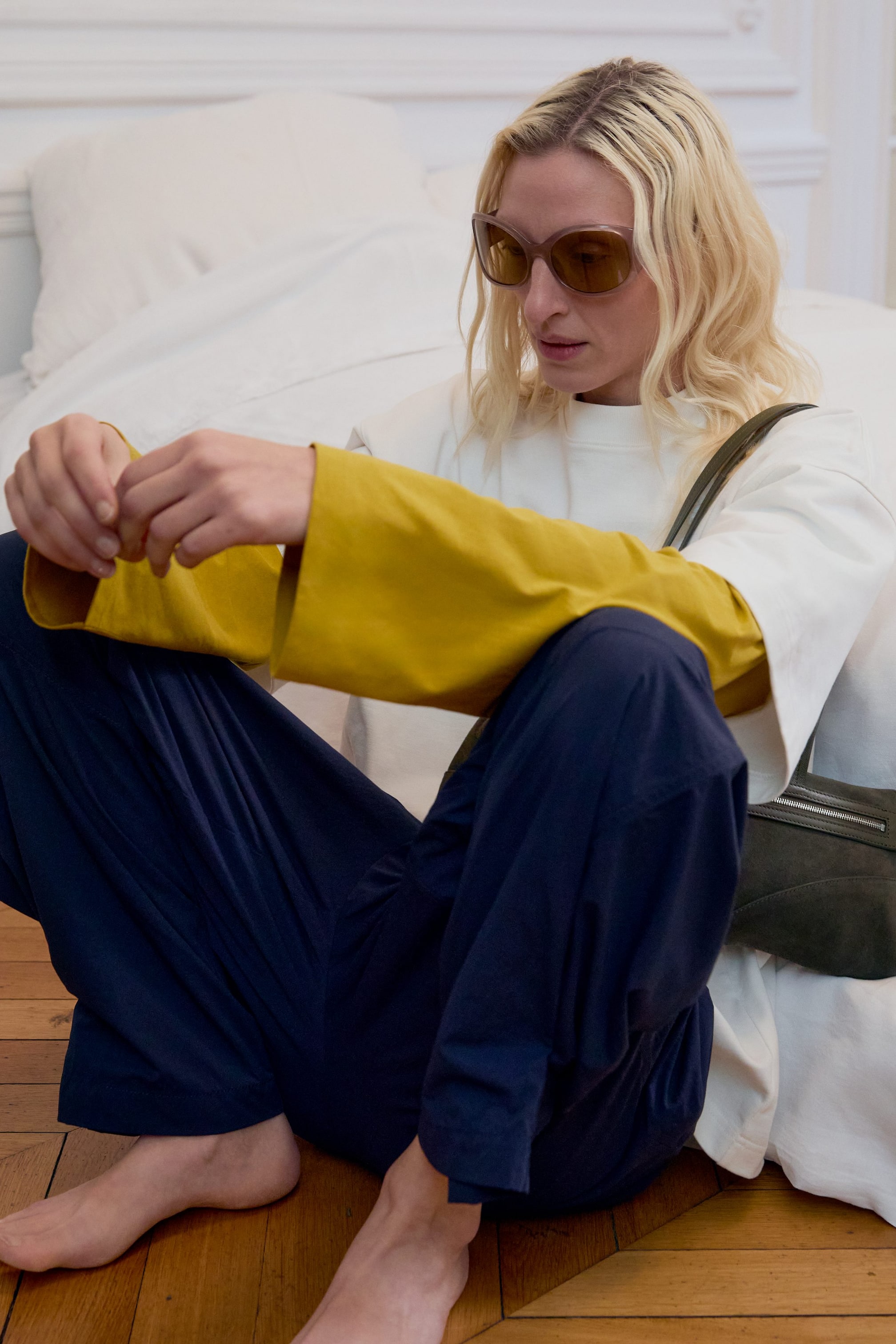 Grösseres Bild ansehen: Ein senfgelbes Langarmshirt wird unter einem weißen Oberteil getragen. Es zeichnet sich durch weite, fließende Ärmel aus, die über die Handgelenke der Trägerin hinausreichen.