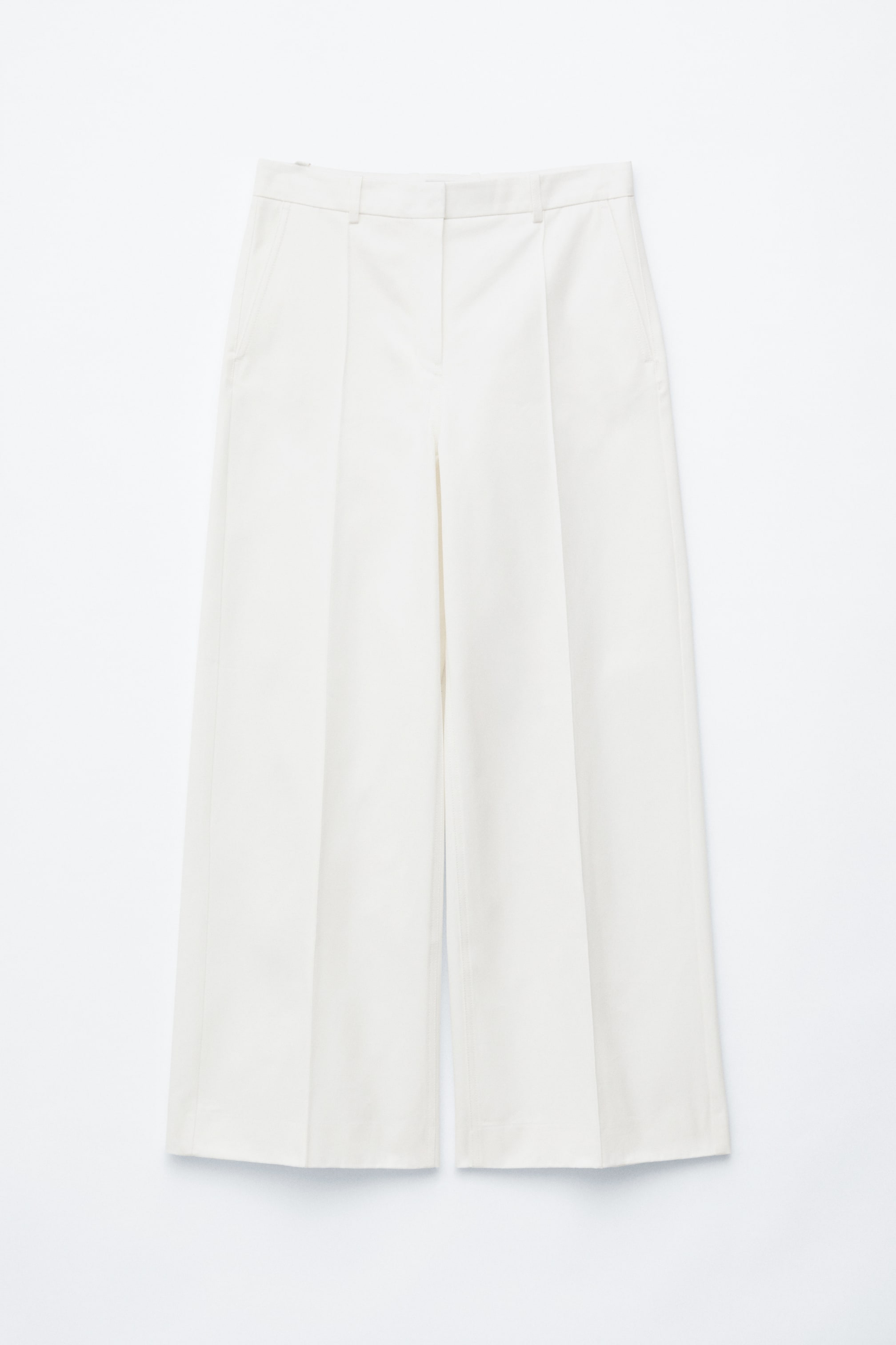 Agrandir l'image: Pantalon blanc cassé présenté de face, avec des jambes larges ornées de plis marqués au centre, une taille plate avec une fermeture visible à crochet et barre, et des poches latérales.