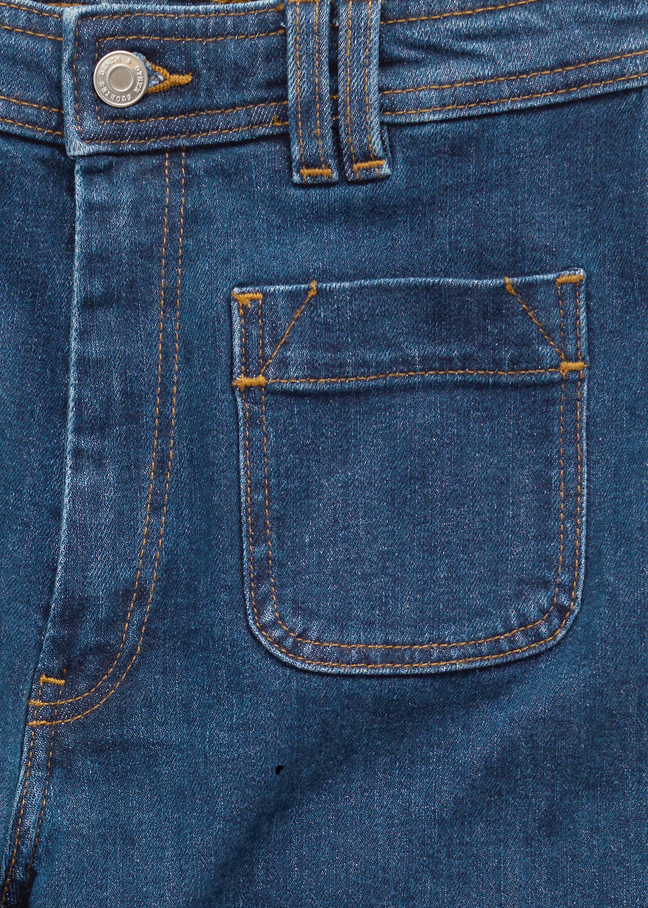 Ingrandisci l'immagine: I jeans blu scuro sono mostrati dalla parte anteriore, con un bottone argentato e una chiusura a zip in vita. Una grande tasca frontale arrotondata è visibile, il tutto accentuato da cuciture a contrasto arancioni e passanti per cintura.