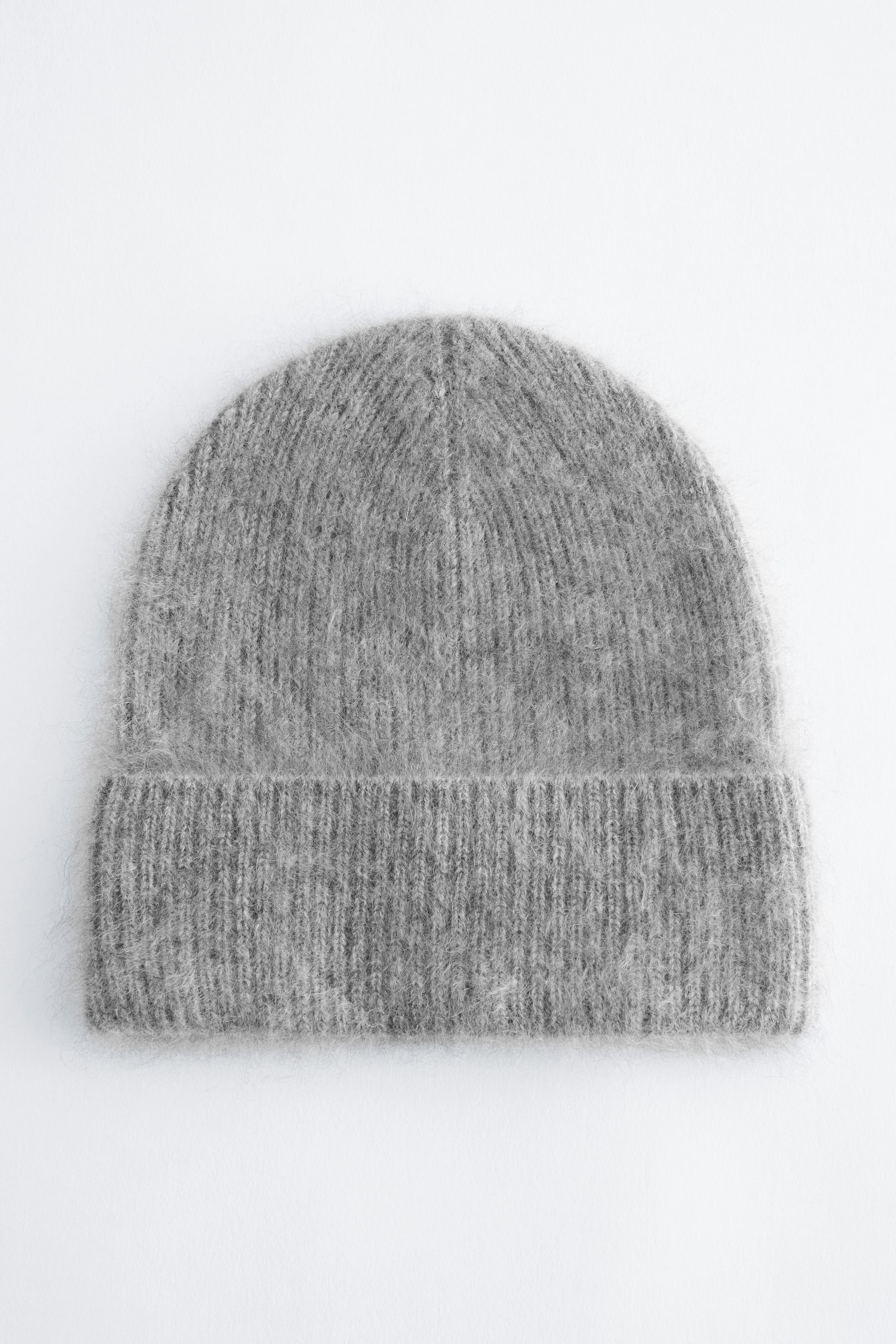 View larger image: A grey knitted beanie is shown from the front, displaying a fuzzy, textured finish with a ribbed knit structure throughout. The hat features a wide, folded-up brim at the base.