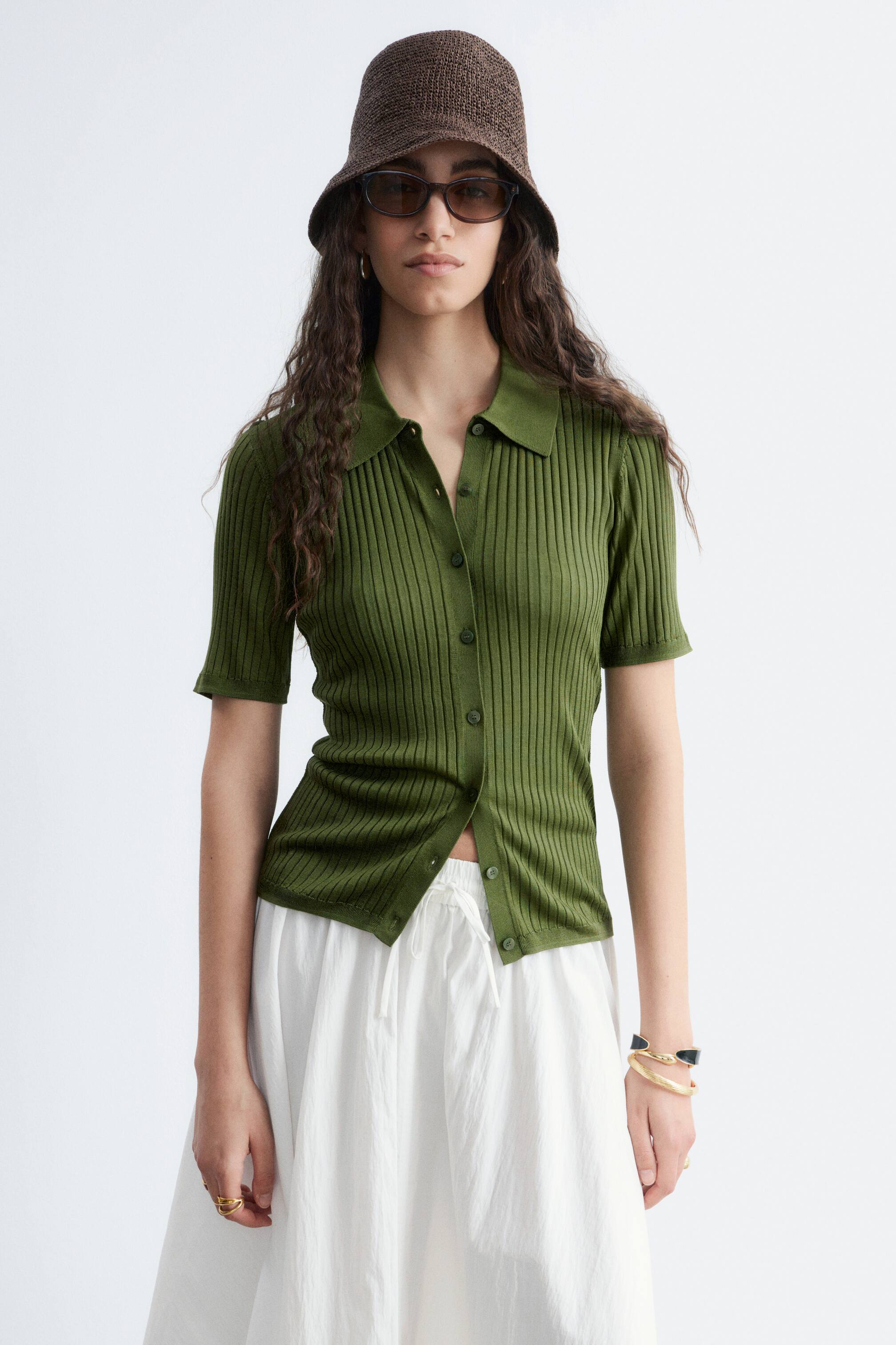 Größeres Bild ansehen: Ein olivgrünes, geripptes Strick-Polohemd mit kurzen Ärmeln wird frontal präsentiert. Es verfügt über einen spitzen Kragen und einen Knopfverschluss vorne. Die unteren Knöpfe bleiben offen.