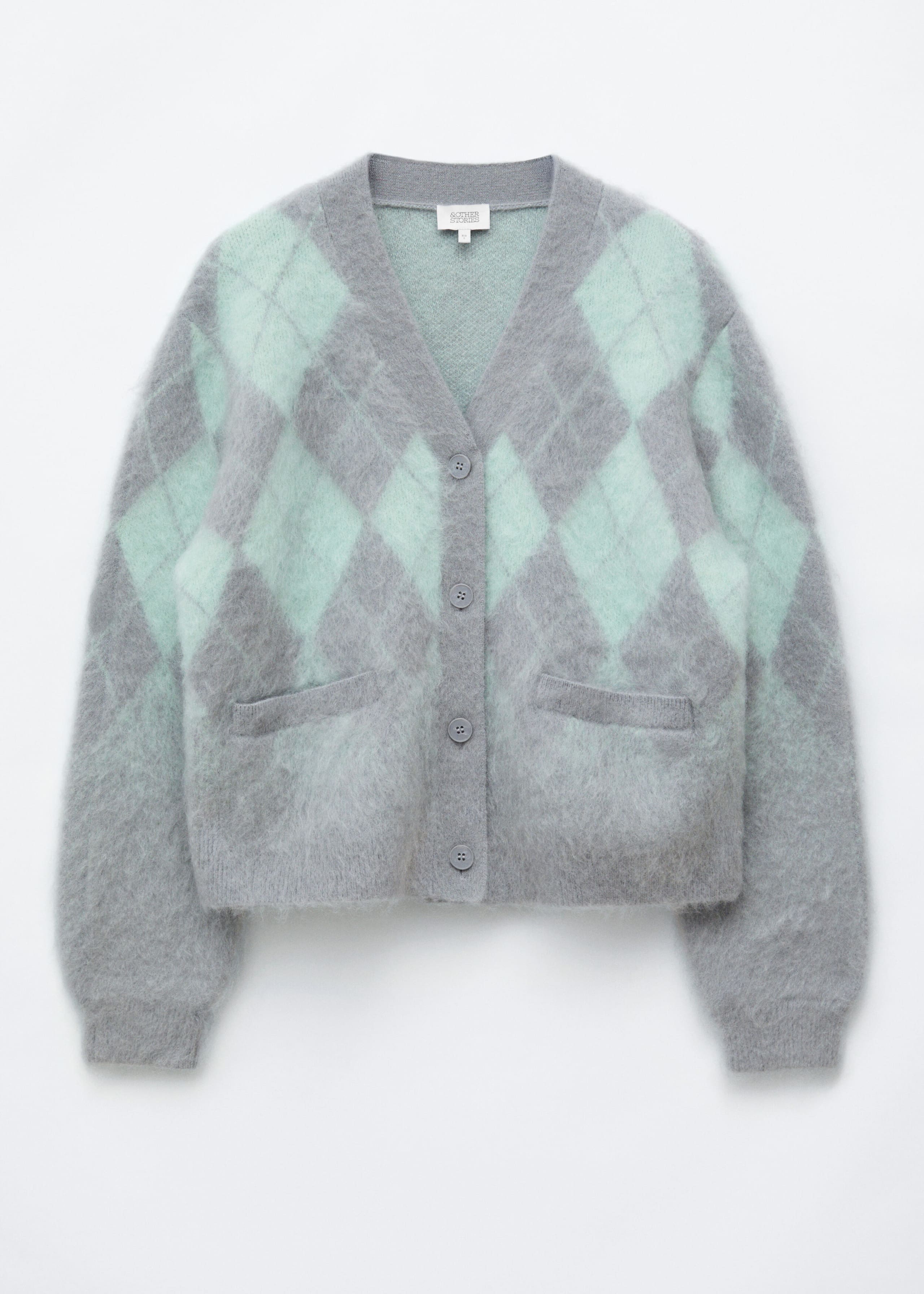 A front-facing mohair-blend argyle cardigan is displayed with a fuzzy, brushed texture and a grey and mint green diamond pattern. The cardigan features a V-neckline, a four-button front closure, two front welt pockets, and ribbed cuffs.