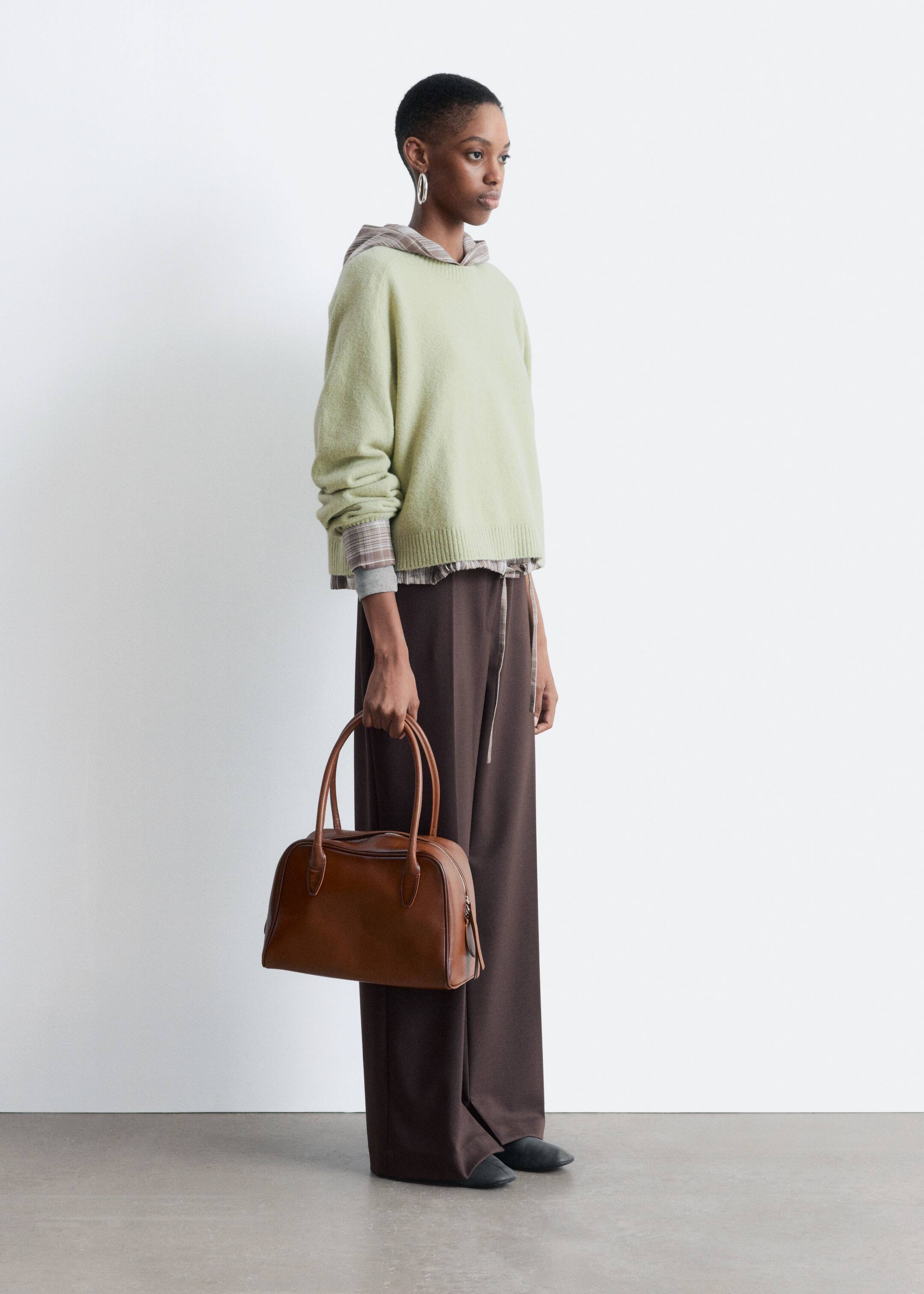 View larger image: A structured brown leather handbag is being presented, facing slightly forward and to the side, showcasing its rectangular body with rounded edges, two top handles, and a visible top zipper closure.