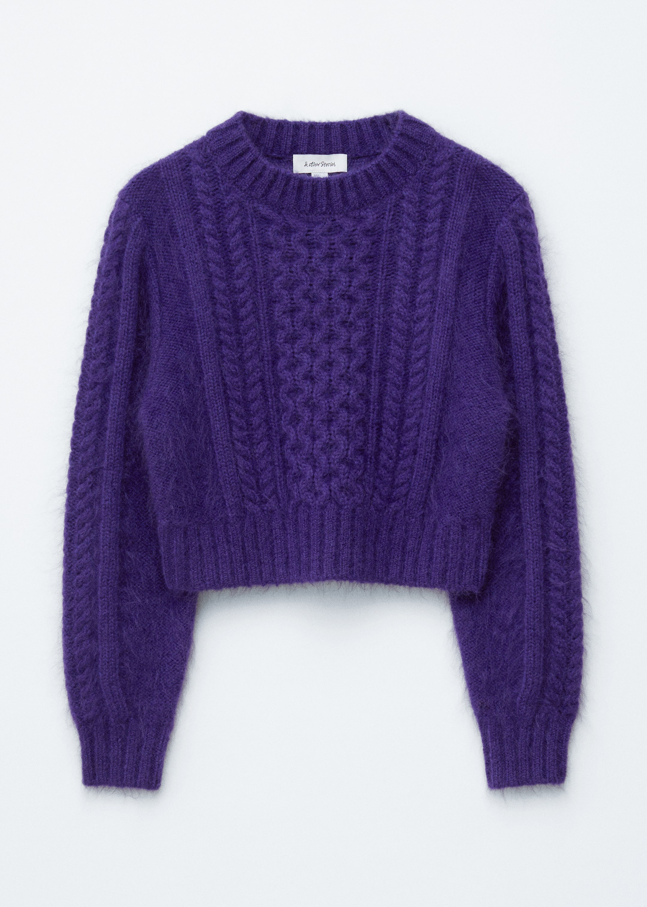 Größeres Bild anzeigen: Ein tiefvioletter, bauchfreier Zopfmuster-Pullover wird von vorne präsentiert, mit einem Rundhalsausschnitt und langen Ärmeln. Er zeigt aufwendige, dicke Zopfmuster über den Körper und die Ärmel und ist mit gerippten Abschlüssen am Ausschnitt, an den Bündchen und am Saum versehen, die eine weiche, flauschige Textur zur Schau stellen.