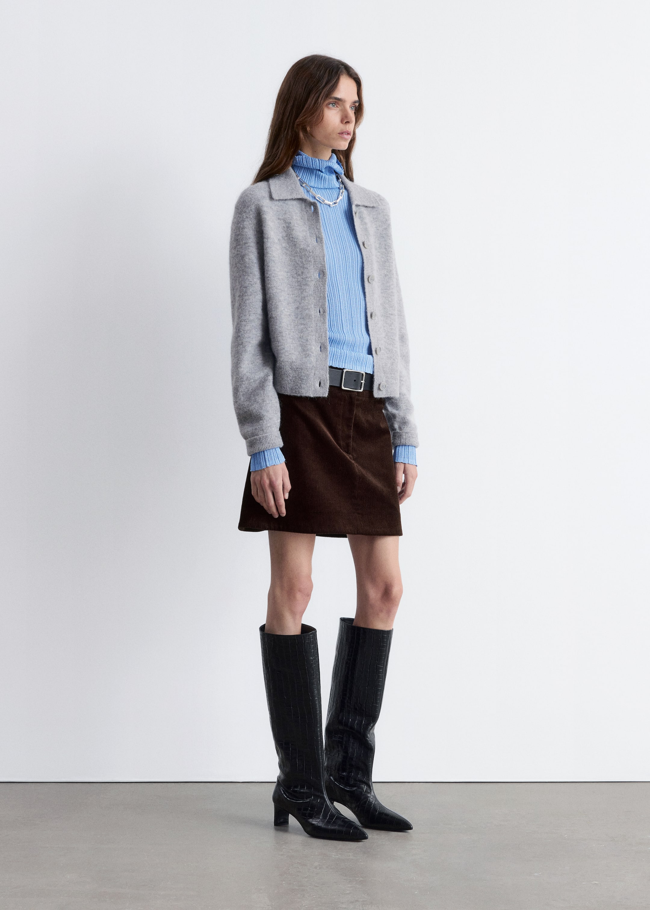 Agrandir l'image: Un cardigan en tricot gris et duveteux est présenté sous un léger angle, mettant en valeur son col plat, sa fermeture à boutons complète et sa coupe décontractée et raccourcie, tout en étant superposé à un col roulé côtelé bleu clair.