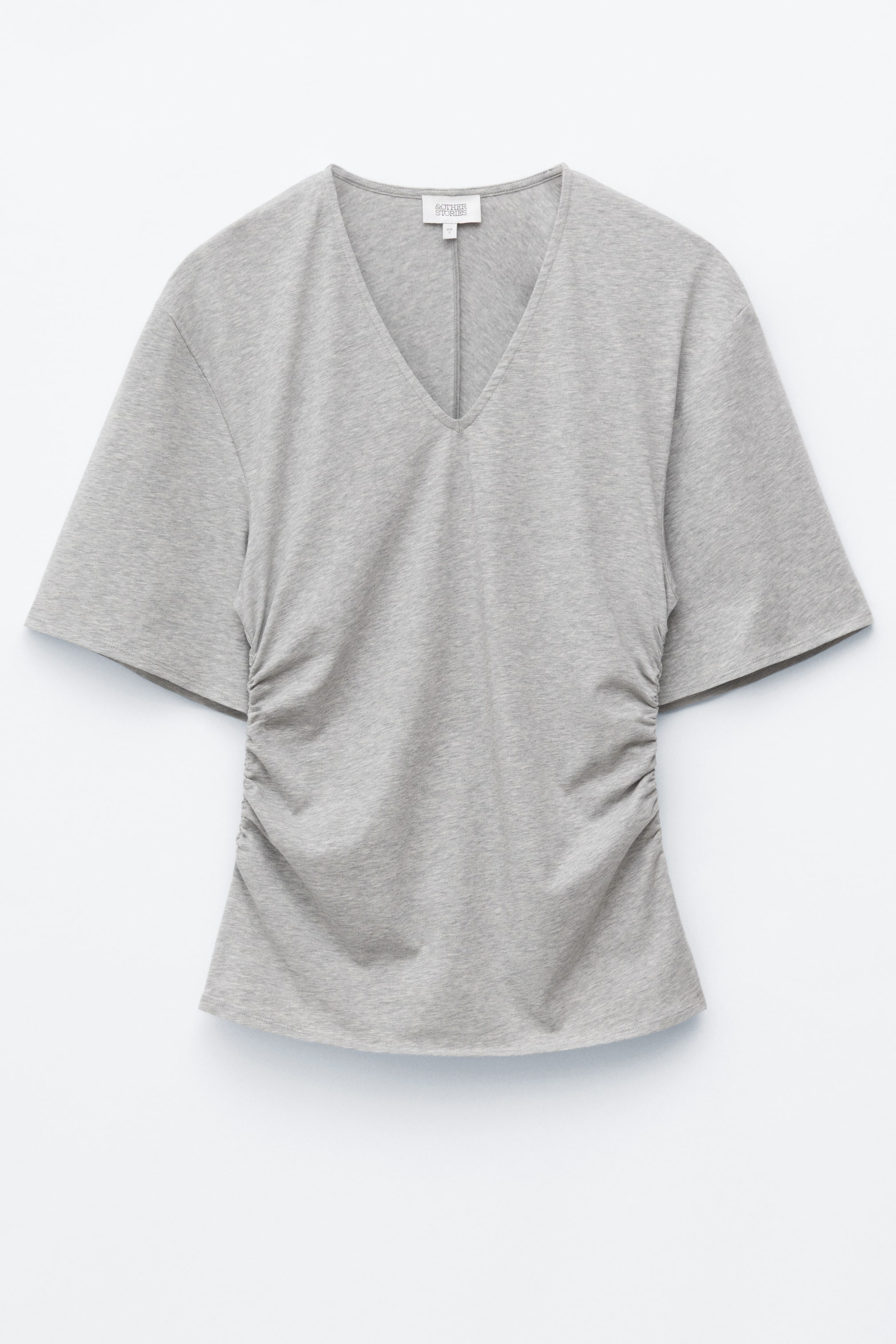 Visa större bild: En ljusgrå V-ringad T-shirt visas framifrån, med breda korta ärmar, rynkor längs båda sidosömmarna och en diskret mittsöm på ryggen.