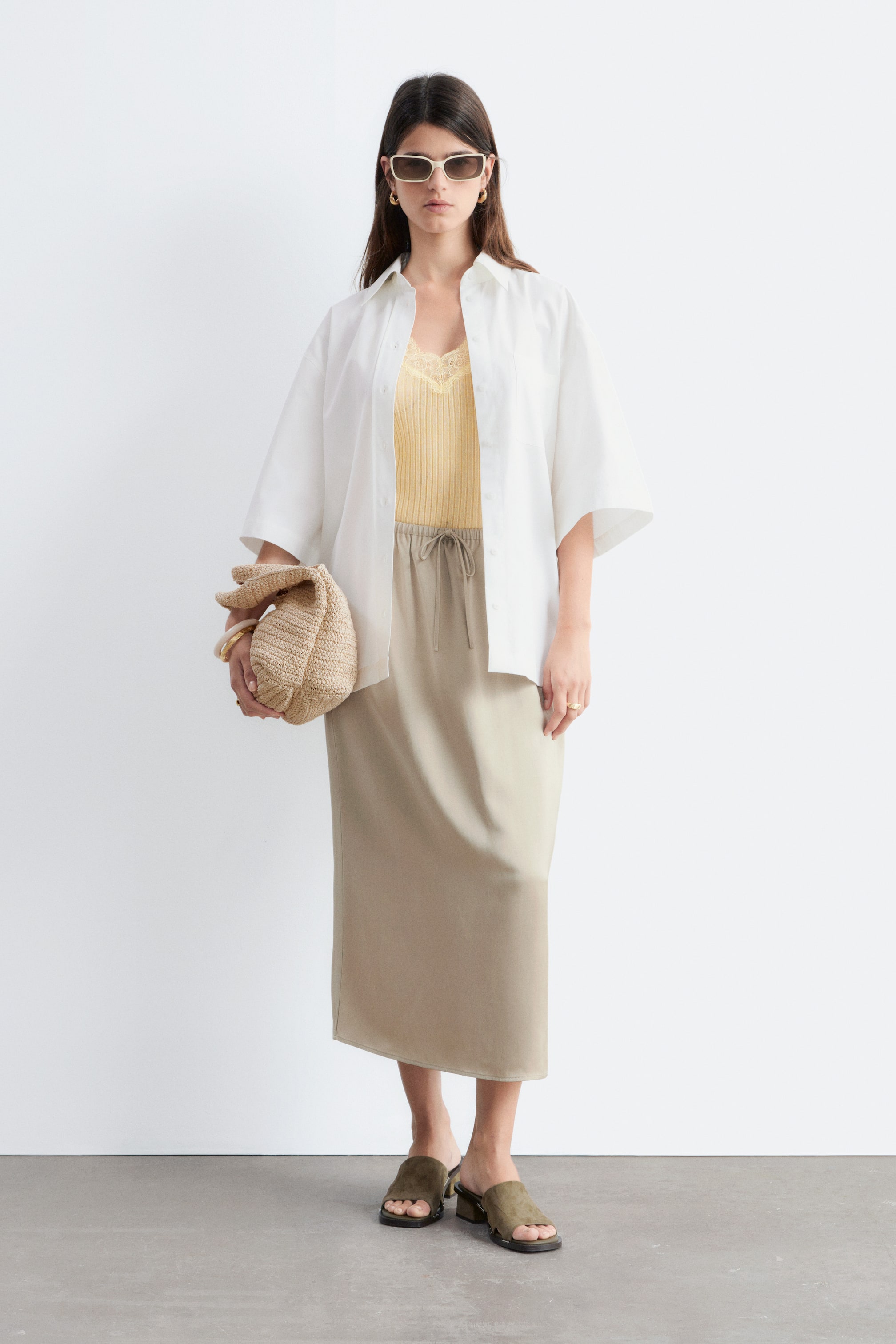 Näytä suurempi kuva: Beige midihame, jossa on suora, laskeutuva leikkaus, ulottuu polvien alapuolelle ja siinä on näkyvä kiristysnauha vyötäröllä ja solmimisnauhat, jotka näkyvät avoimen valkoisen paidan alta.