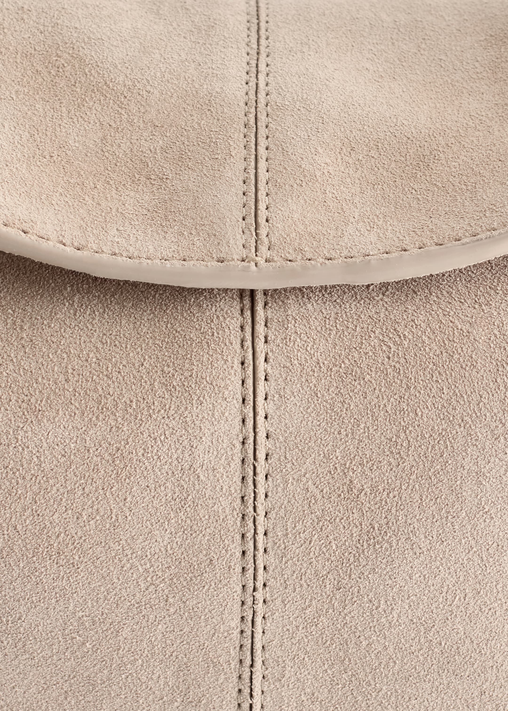 Agrandir l'image: Un gros plan d'un sac en cuir texturé de couleur claire montre une couture verticale. Un rabat courbé avec une finition lisse est visible sur le dessus.