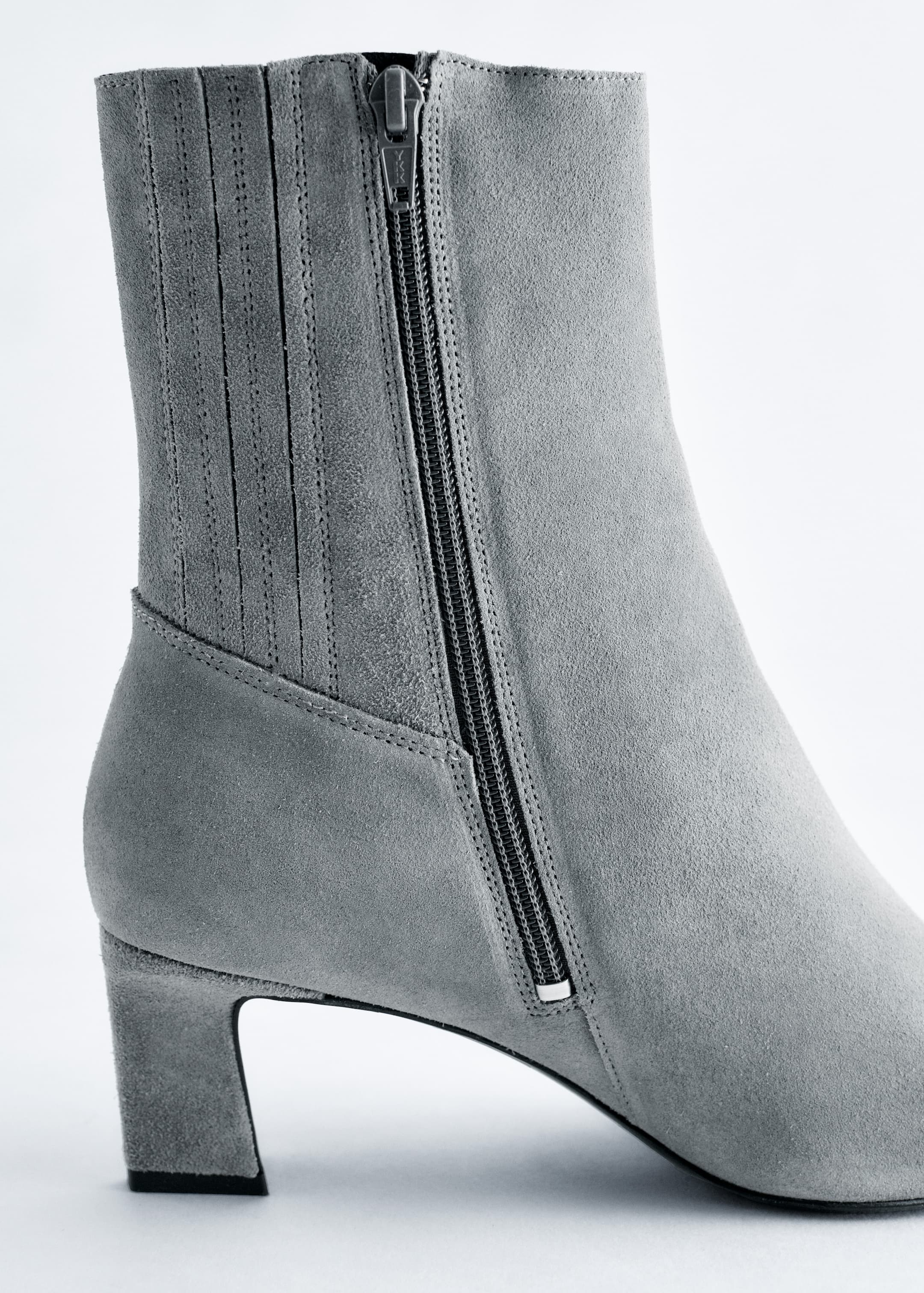 View larger image: A grey suede ankle boot is angling to the left, showcasing its right side. A black zipper is running vertically along the outer side of the boot shaft, which is detailed with multiple parallel vertical stitched lines. The boot is featuring a distinctive pointed toe and a neat kitten heel.