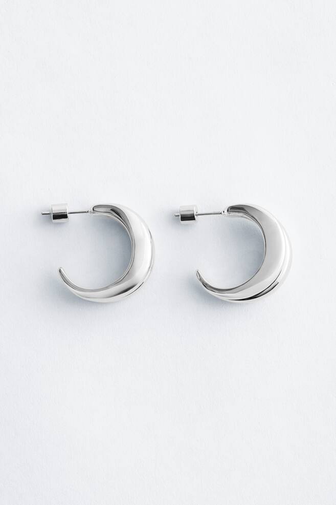 A pair of silver-toned double-hoop earrings featuring a thick, crescent shape with a polished finish and a pin fastening at the top. - 1