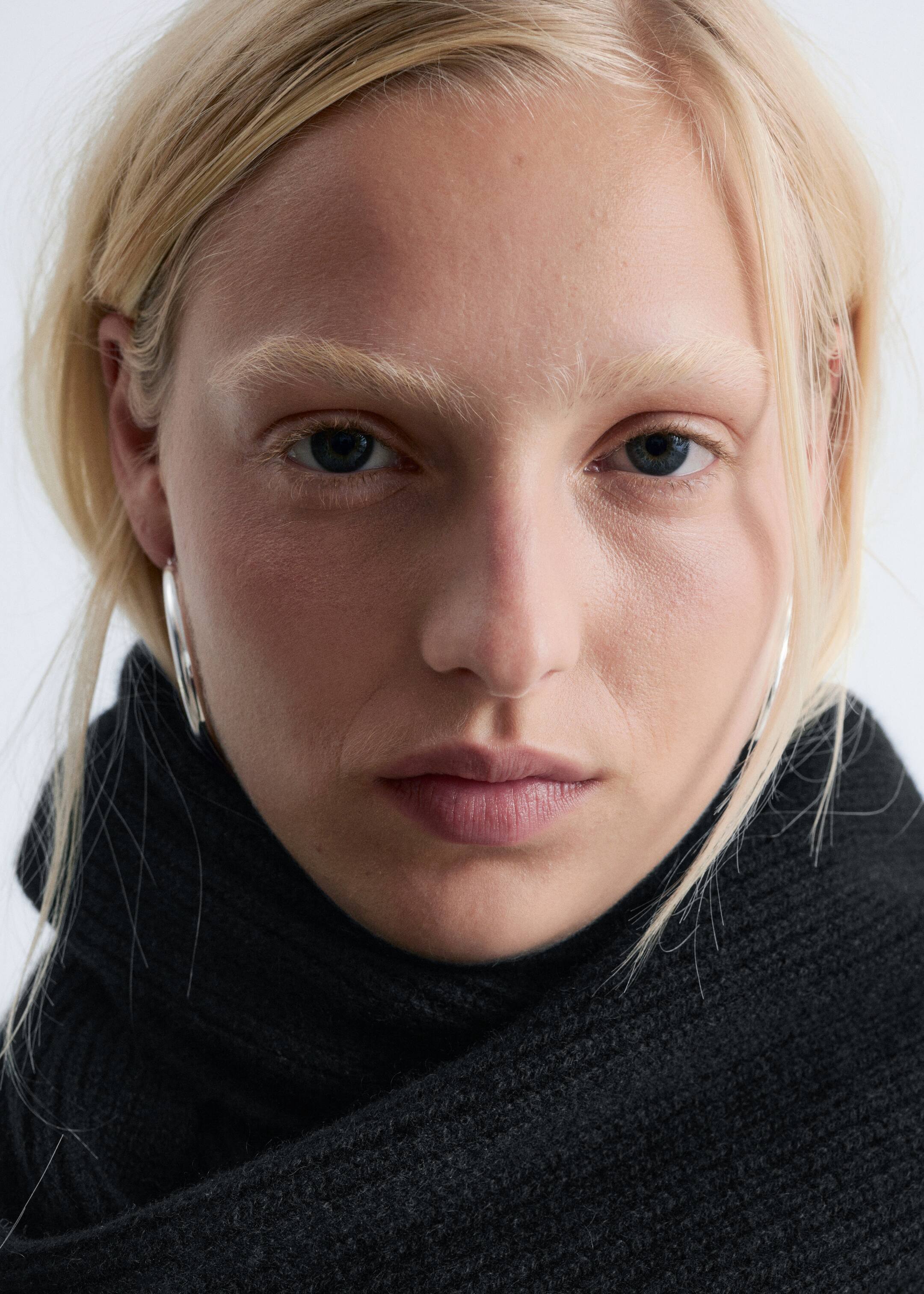 Größeres Bild anzeigen: Ein weicher, schwarzer Kaschmir-Strickschal mit gerippter Oberfläche wird von dem Model getragen. Er ist um ihren Hals gewickelt und bedeckt den unteren Teil ihres Gesichts.