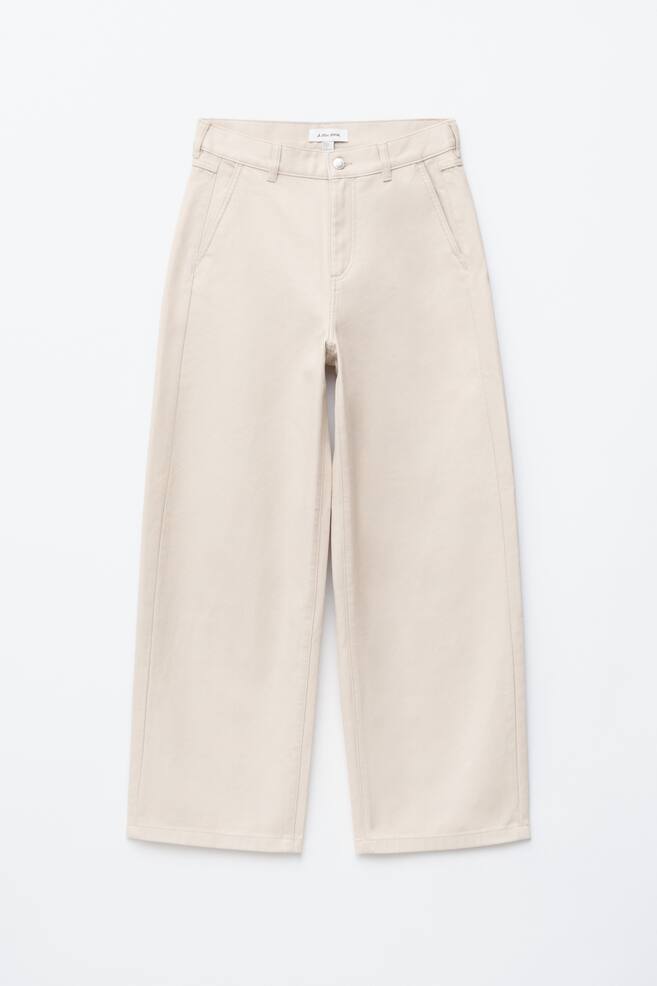 Pantalones de pierna ancha en color crema se exhiben desde el frente, con cierre de botón y cremallera, trabillas para cinturón y bolsillos delanteros inclinados. Los pantalones están diseñados con costuras tonales visibles en toda su extensión. - 1