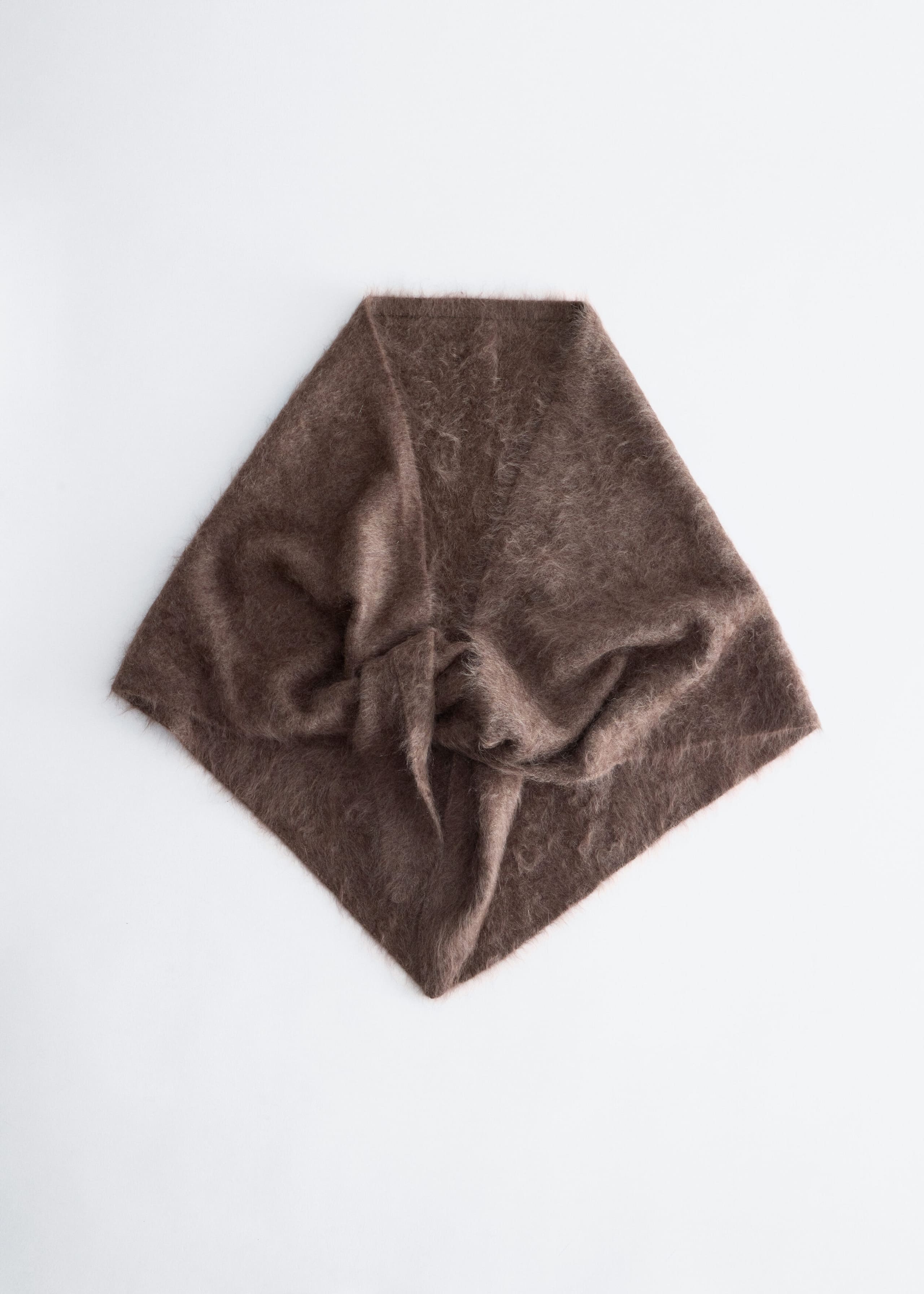 A brown brushed-knit scarf is laid flat, showing off its fuzzy, textured surface and gathered drape at the center. The product faces forward, highlighting a triangular structure with soft, folded layers.