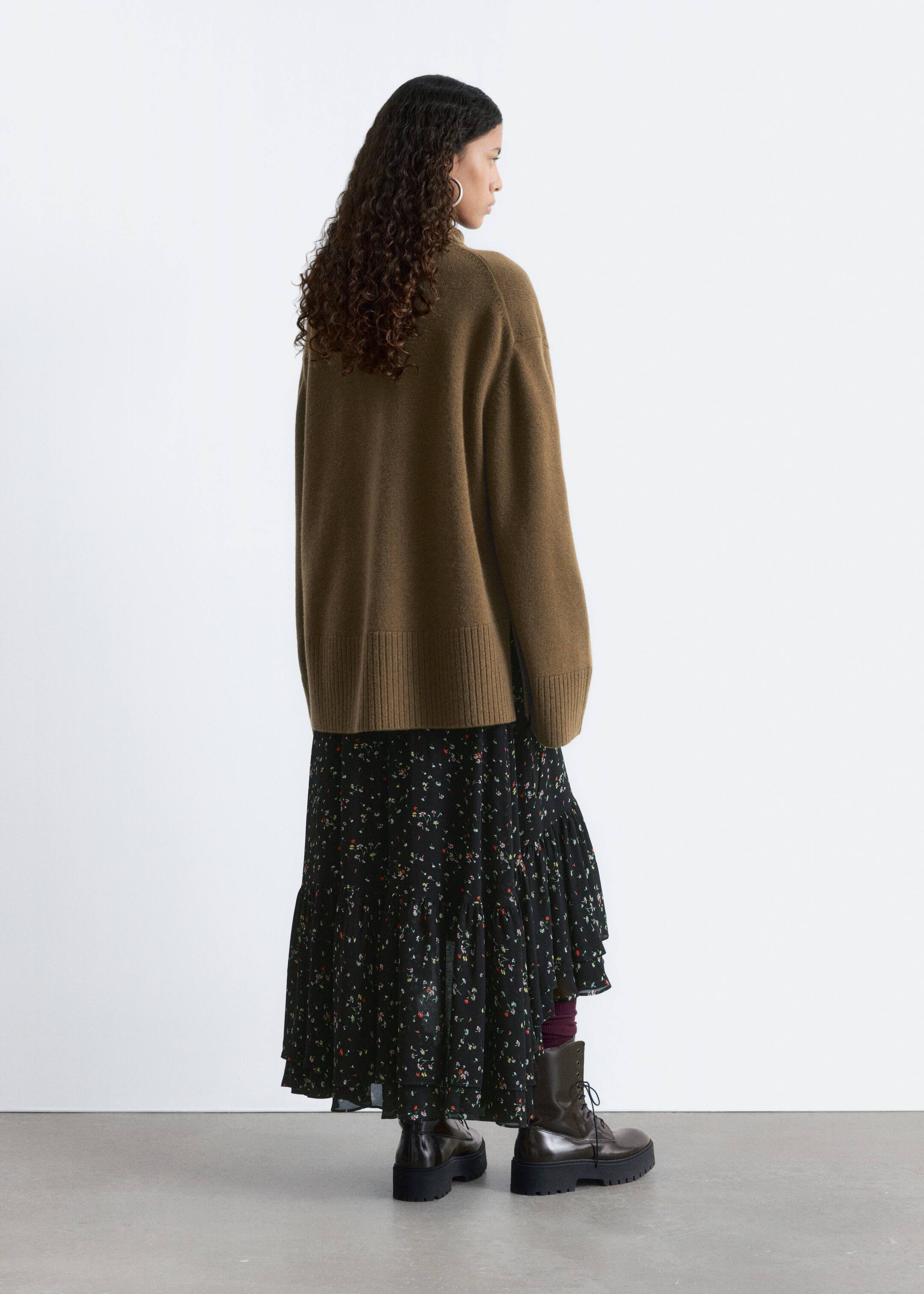 Agrandir l'image: Un pull marron ample, doté de poignets côtelés et d'un ourlet côtelé, est porté superposé à une jupe midi noire. La jupe présente un petit imprimé floral multicolore et un design fluide et à volants avec un ourlet irrégulier. Les vêtements sont présentés de dos.