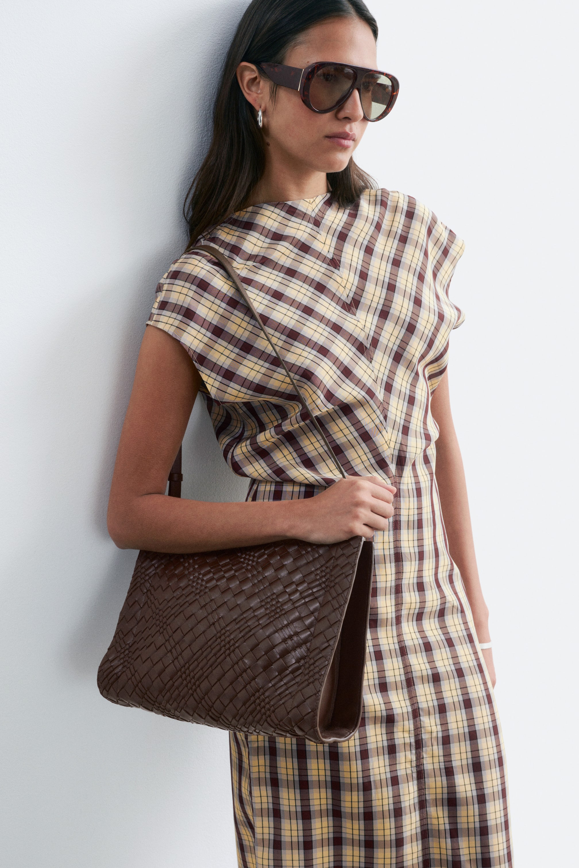 View larger image: A dark brown woven bag with a distinctive criss-cross pattern is being held in a hand, presenting a soft, somewhat flat structure.