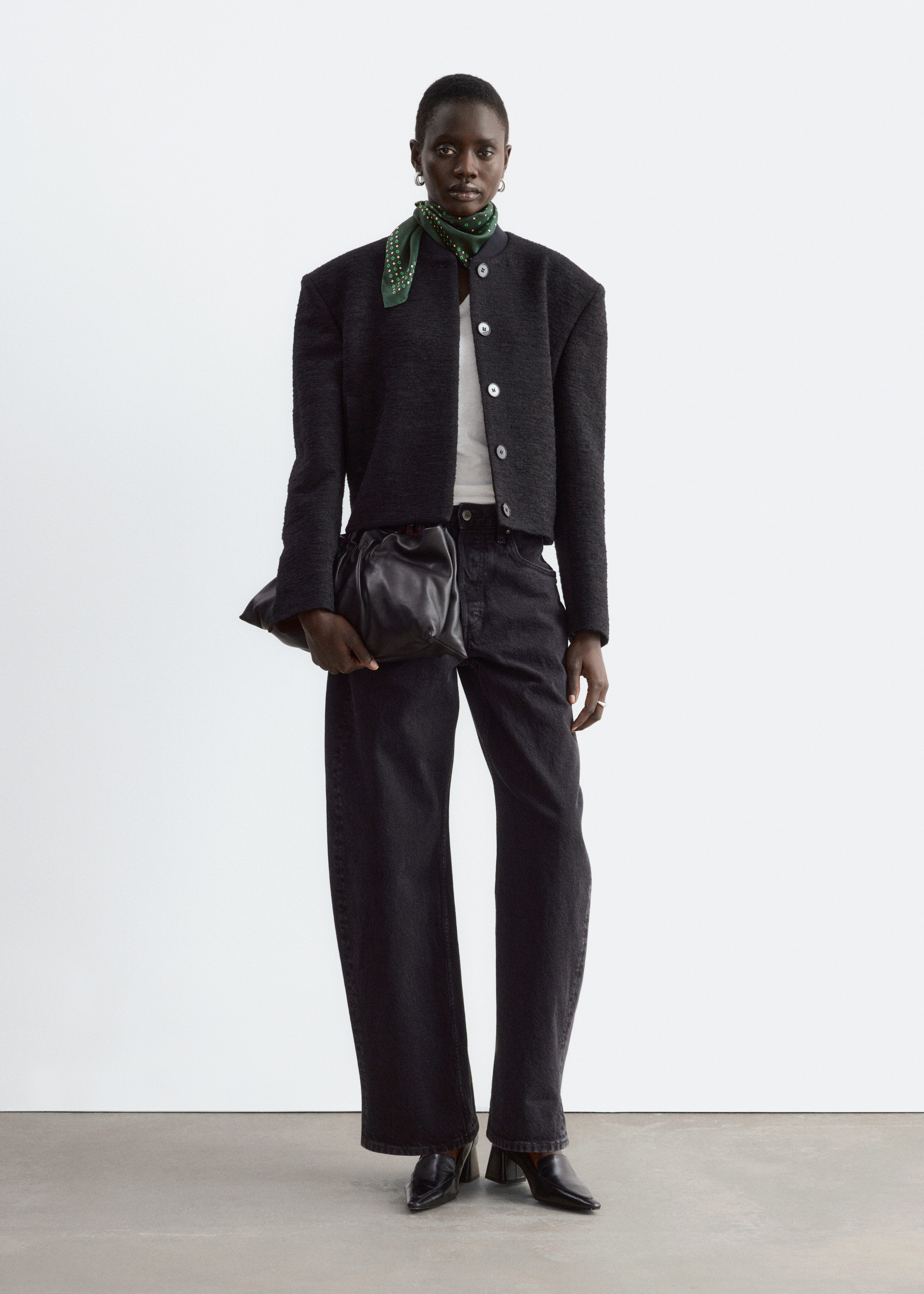 Una giacca bomber in tweed grigio scuro Ã¨ mostrata frontalmente, mettendo in evidenza la silhouette corta, le spalle strutturate e il tessuto ÑÐµÐºÑÑurizzato. Presenta un colletto a coste, una chiusura frontale con bottoni nascosti e un solo bottone superiore visibile, oltre a sottili tasche a filetto.