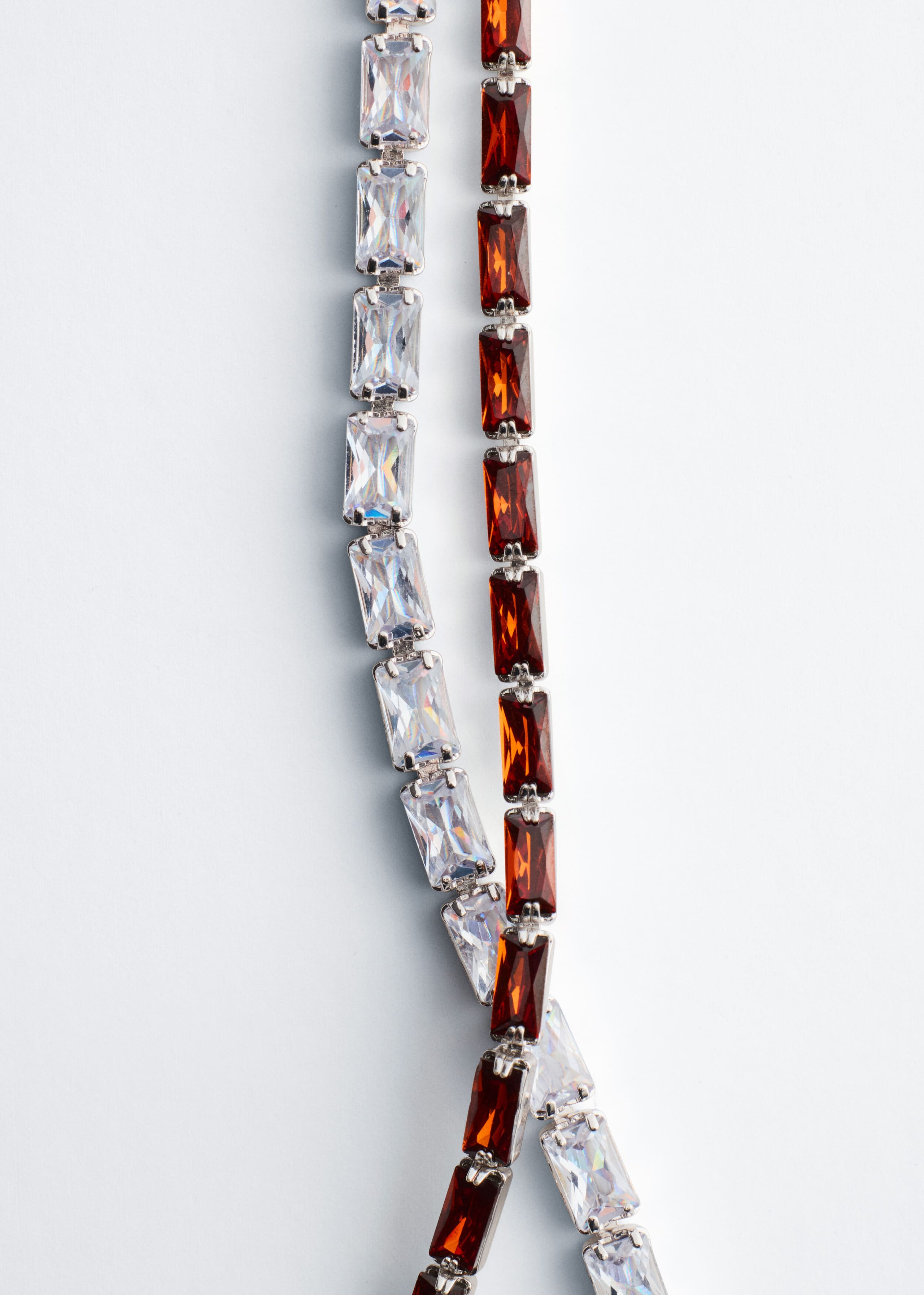 Two variations of the tennis choker necklace are draped vertically, with one featuring clear, rectangular-cut cubic zirconia stones and the other featuring amber-colored, rectangular-cut stones. Both chains are crafted with silver-tone prong settings and are shown crossing over each other at the bottom.