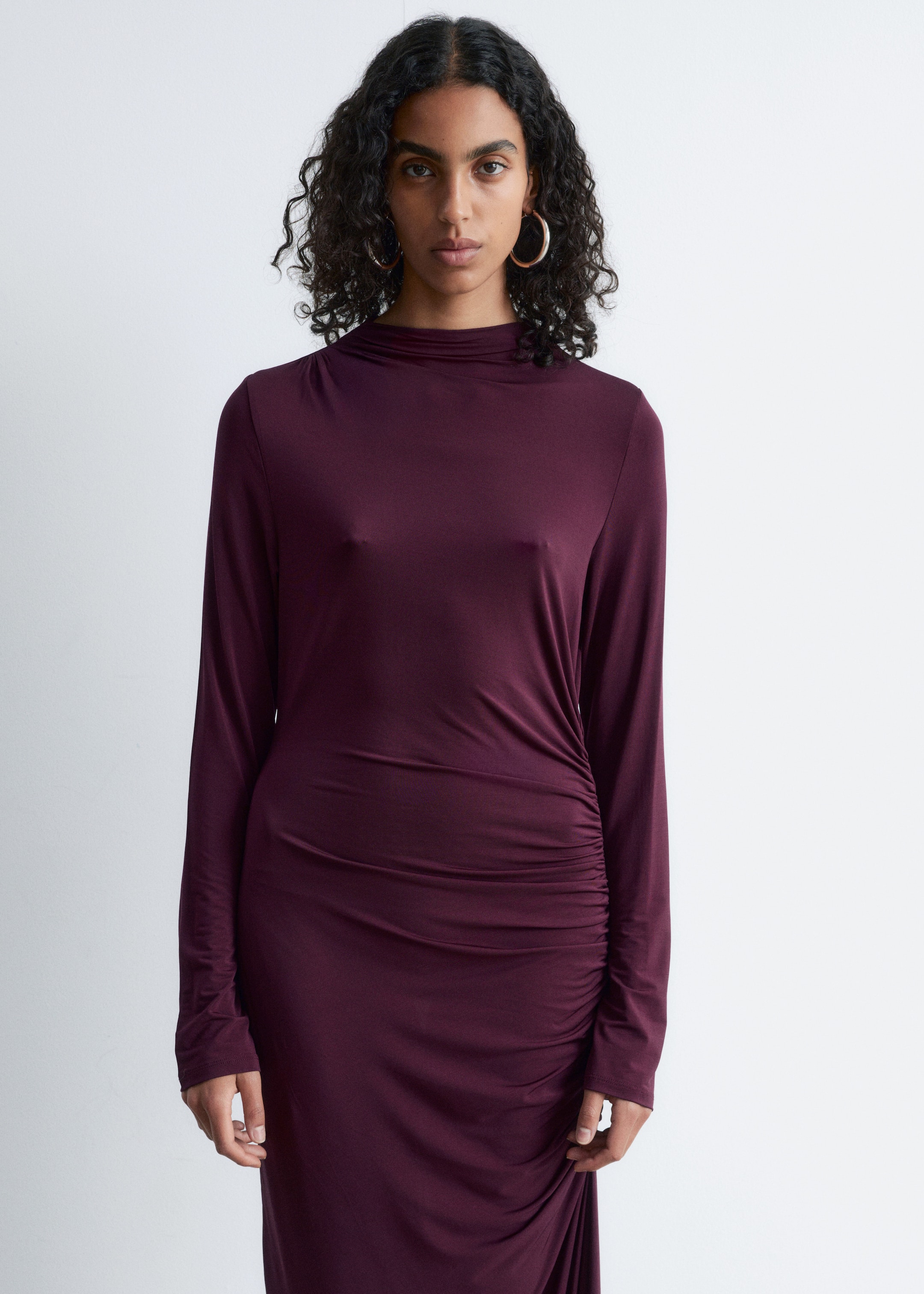 Größeres Bild anzeigen: Ein dunkelrotes, figurbetontes Kleid wird vorwärts präsentiert, mit einem hohen, drapierten Ausschnitt und langen Ärmeln. Das Kleid zeigt Raffungen entlang seiner rechten Seite, die einen drapierten Effekt auf dem Rock erzeugen.