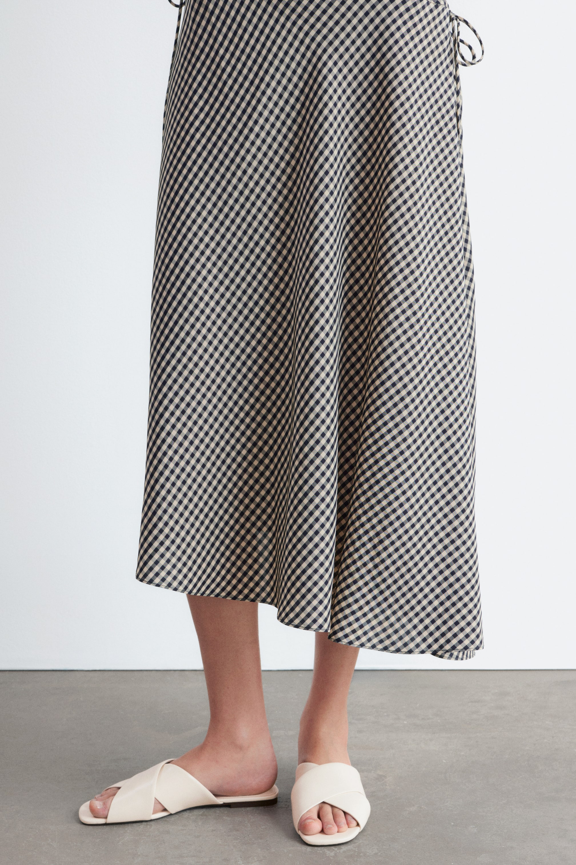 Visualizza immagine più grande: La gonna midi presenta un motivo a quadri in blu scuro e beige, scorrendo dolcemente con un dettaglio di fiocco visibile sul lato destro.