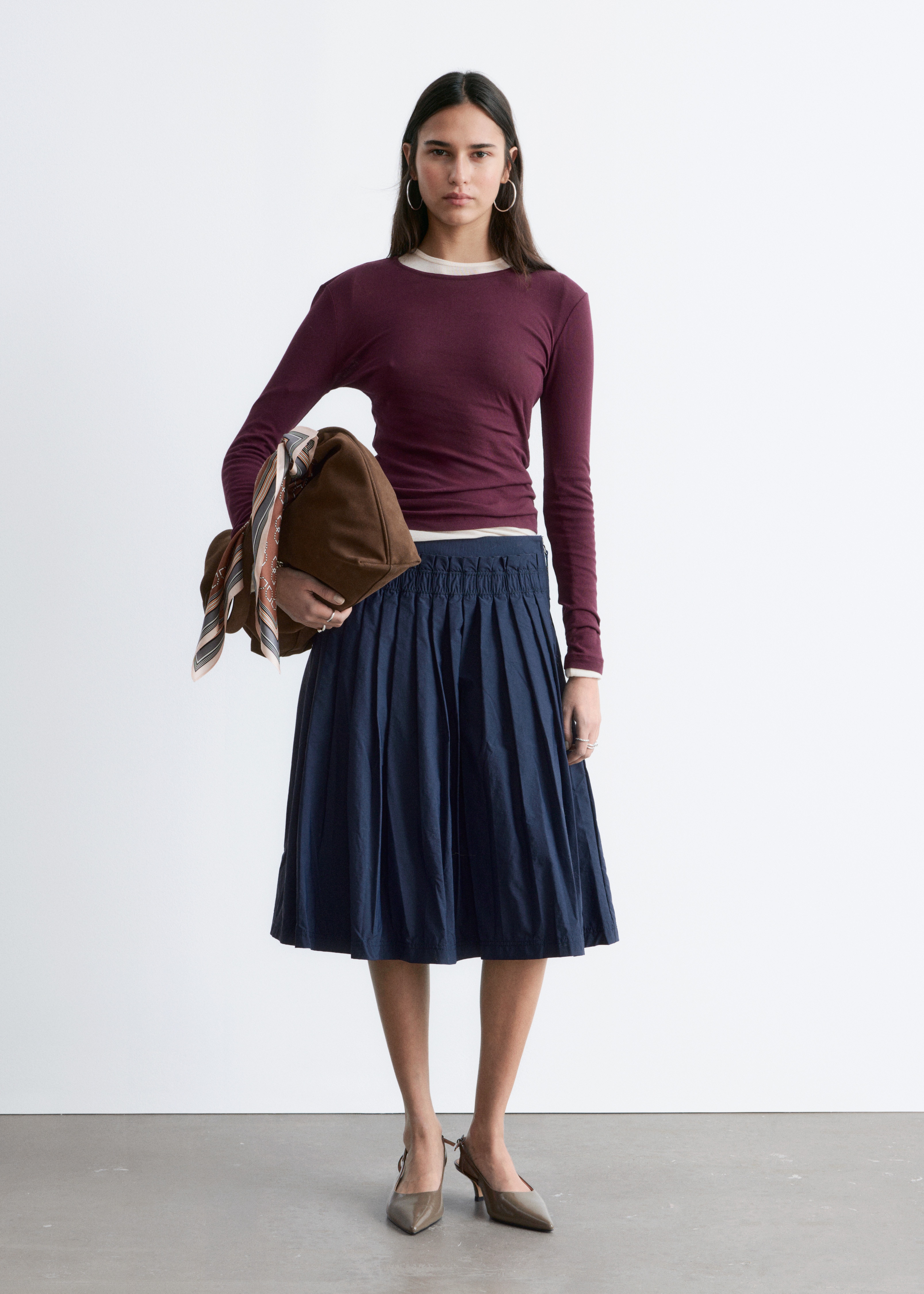 Un top a maniche lunghe color bordeaux mostra il davanti, con scollo rotondo e silhouette slim fit. È realizzato in tessuto jersey liscio.