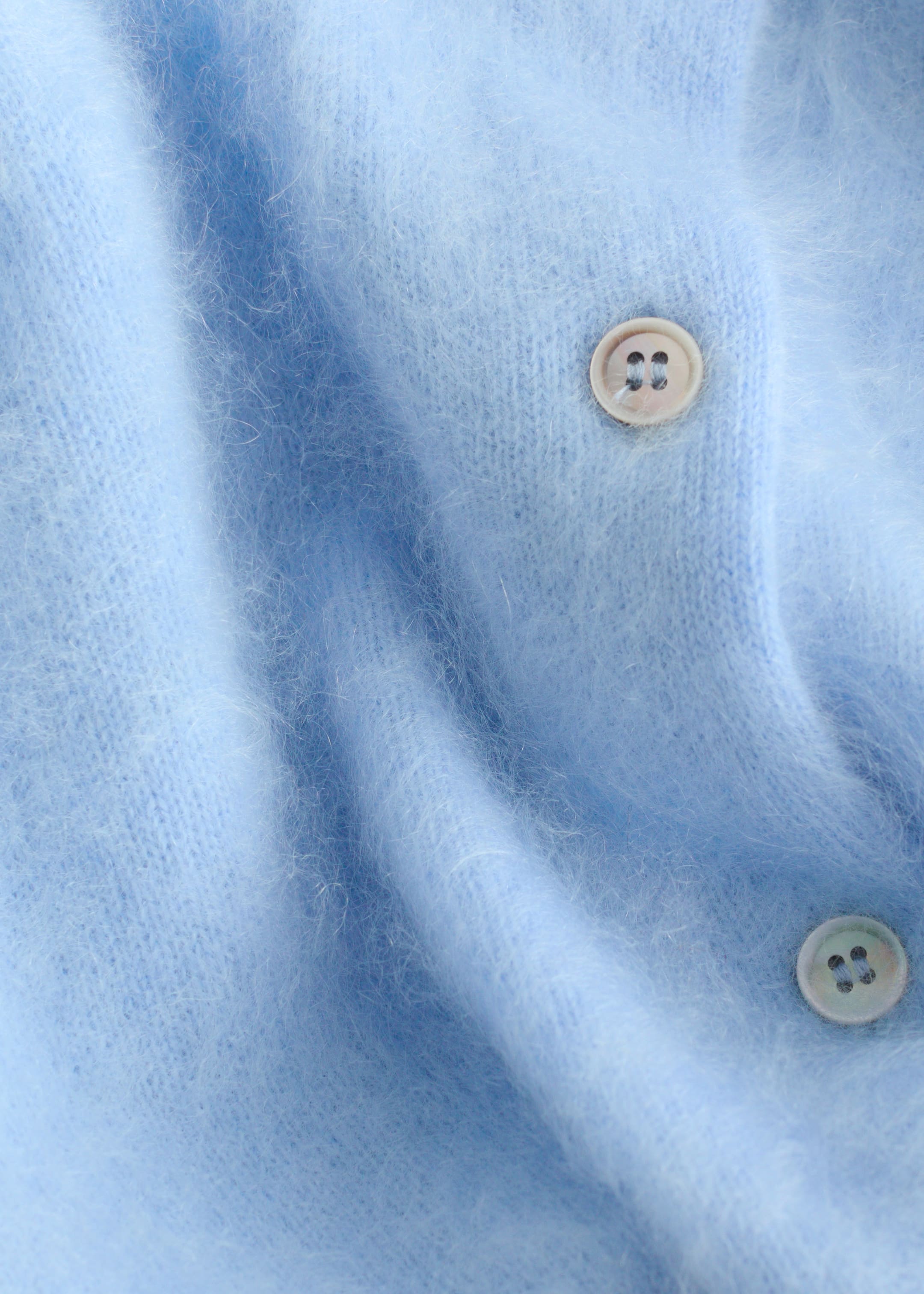 Visualizza immagine più grande: Un cardigan in cashmere lavorato a maglia di colore azzurro chiaro mostra la sua texture morbida e soffice e due bottoni a quattro fori di colore chiaro sulla sua abbottonatura anteriore, con il tessuto che cade dolcemente.