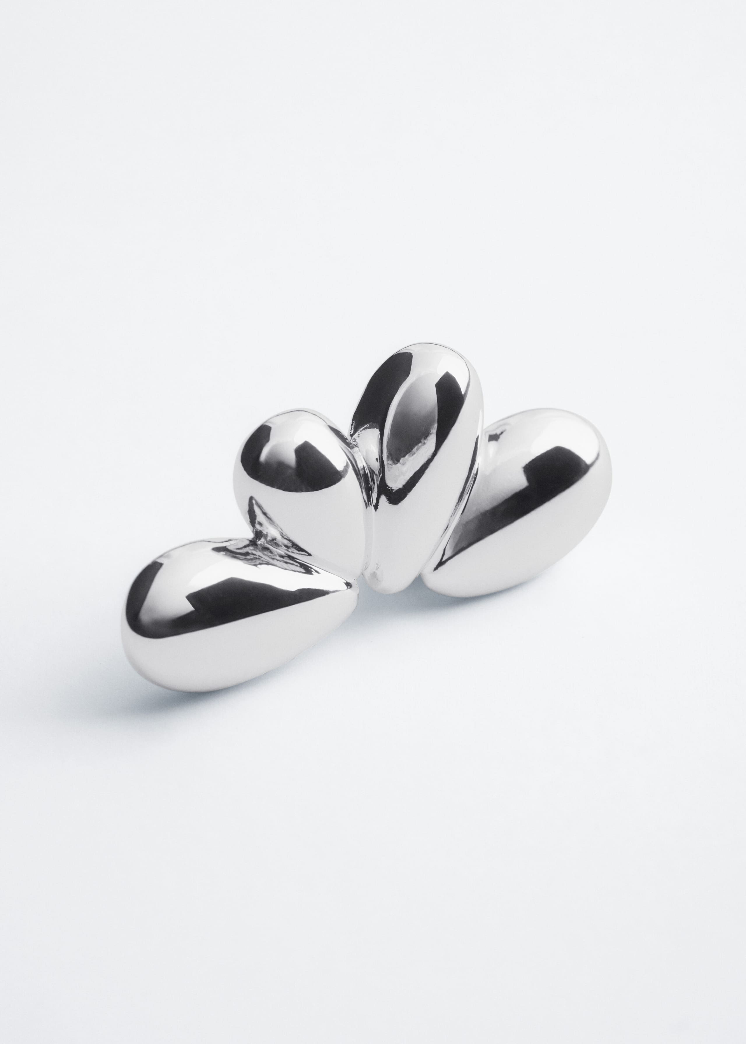 A set of polished silver-toned sculptural earrings is resting together, showcasing their smooth, organic, teardrop-like shapes. The pieces feature a highly reflective, mirror-like finish, highlighting their rounded, bulbous forms from a front three-quarter angle.