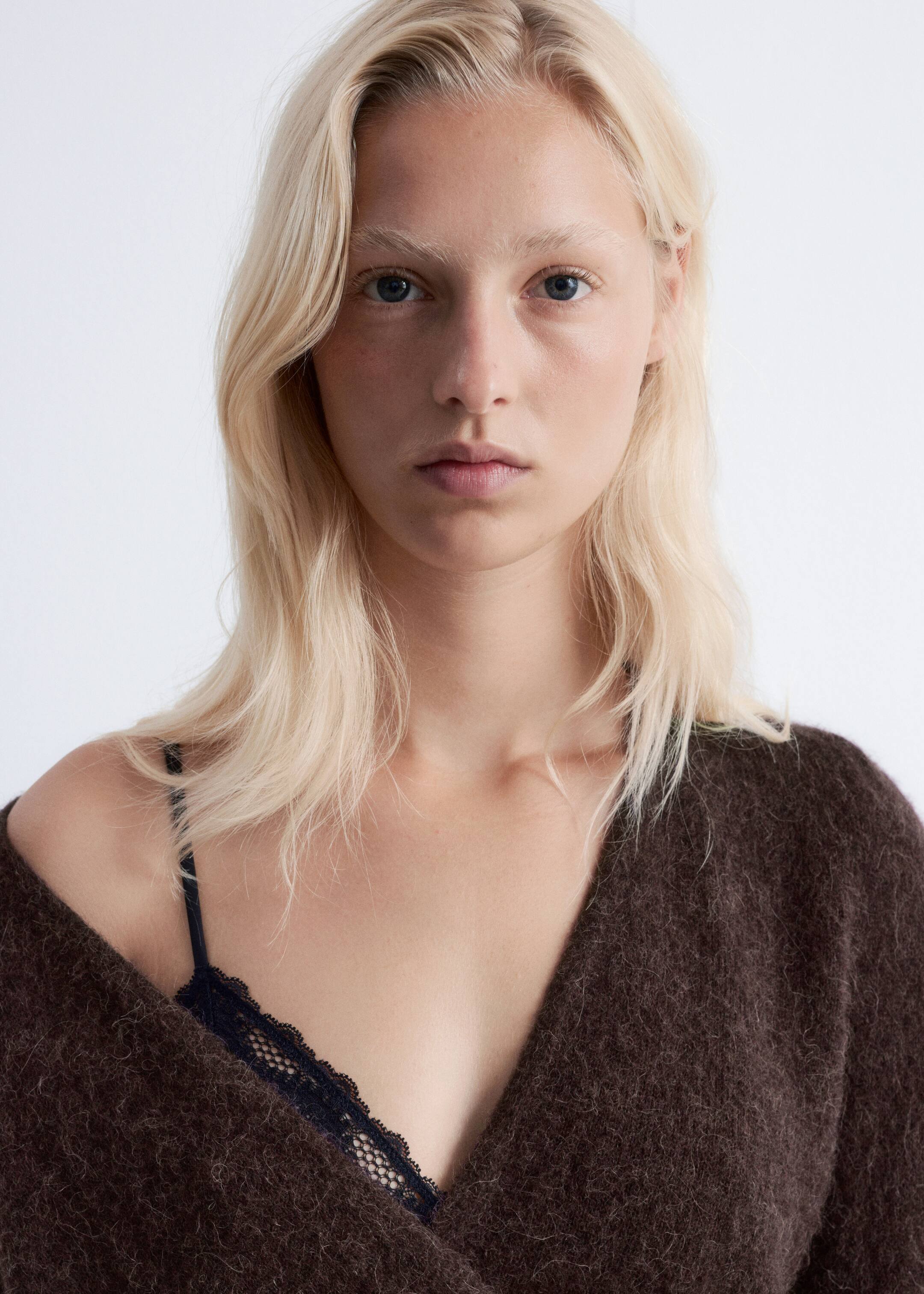 Ingrandisci l'immagine: La modella indossa un cardigan avvolgente marrone scuro e peloso, che rivela un reggiseno a triangolo in pizzo nero sotto.
