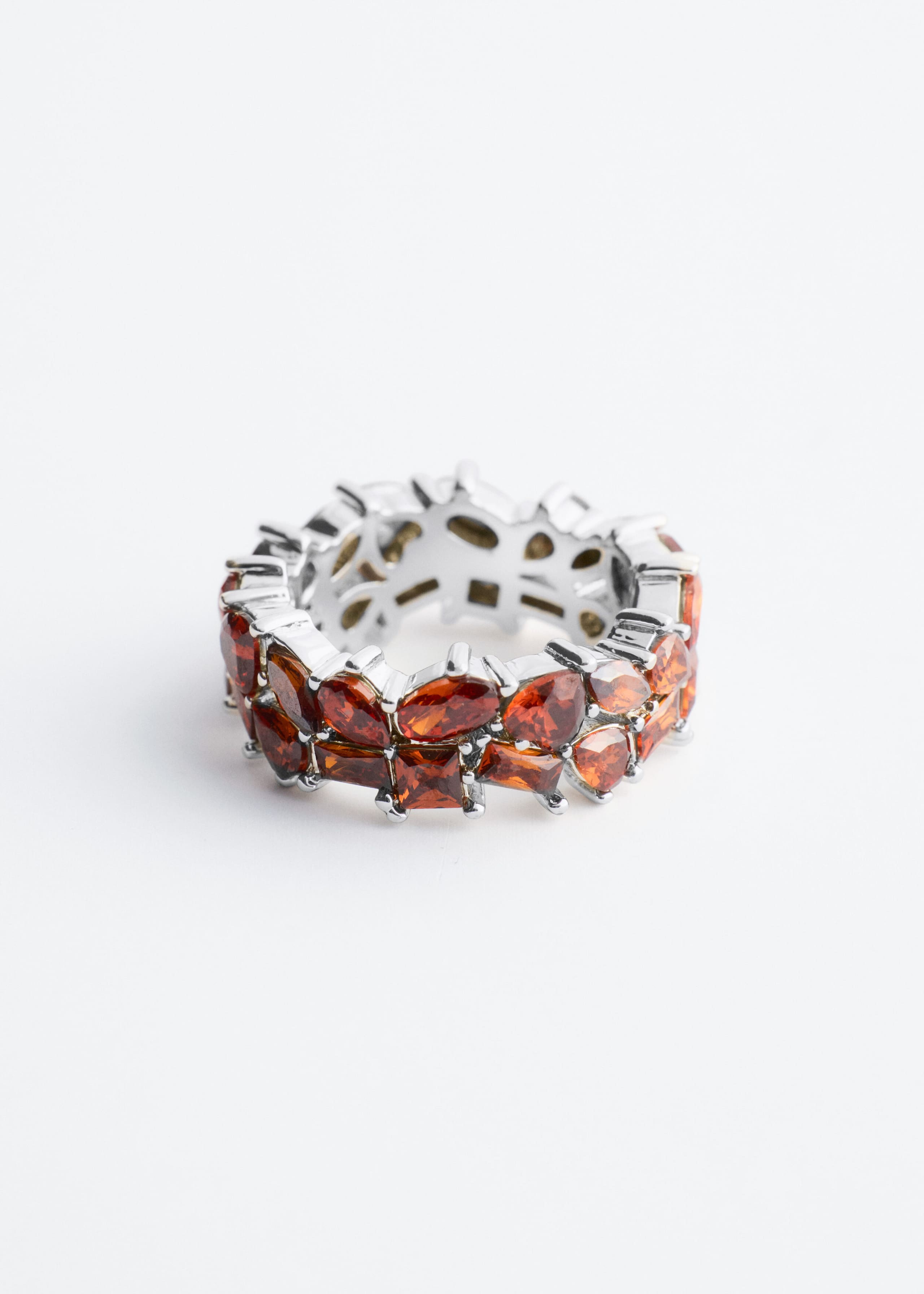 A silver-toned eternity ring is standing upright, featuring two rows of prong-set amber-orange gemstones. The top row displays marquise-cut stones, while the bottom row showcases smaller square-cut stones, all set in a polished white metal band.