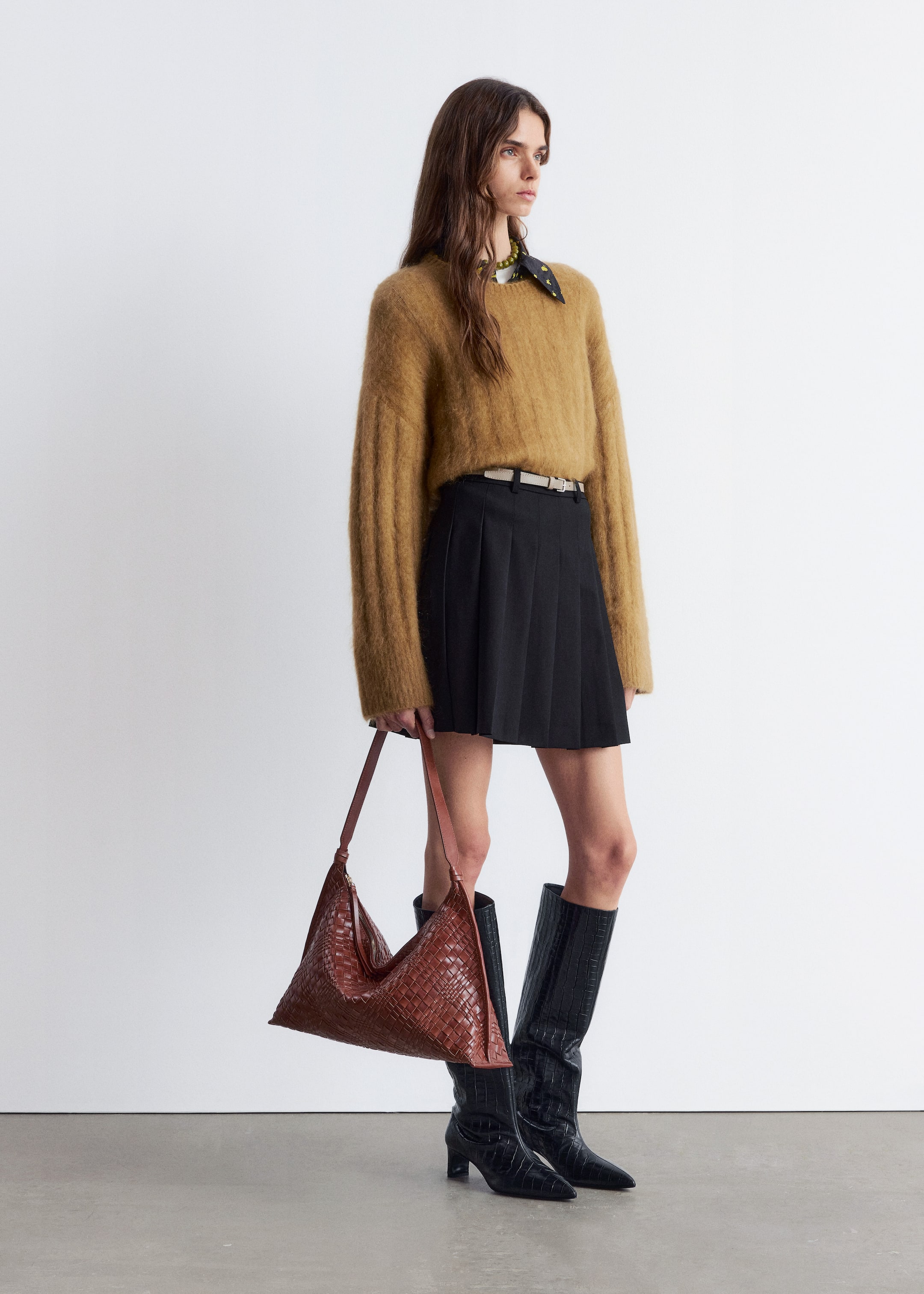 Agrandir l'image: Un sac tissé brun est tenu par sa seule sangle, mettant en valeur sa forme souple et non structurée de hobo. Son corps présente un motif tissé distinct et complexe.