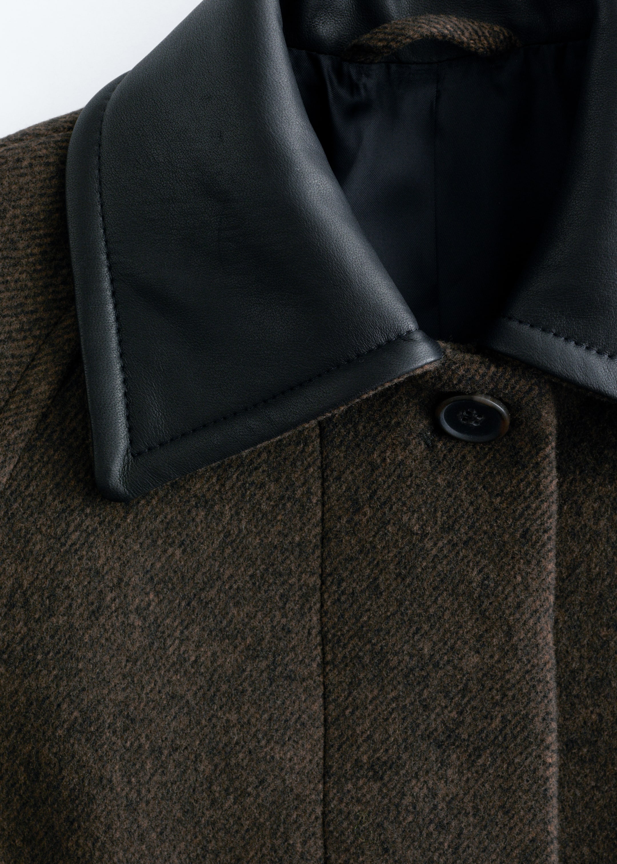 View larger image: A brown wool-blend coat is displaying a contrasting black leather collar with visible stitching, and a single dark button is fastening its concealed placket.