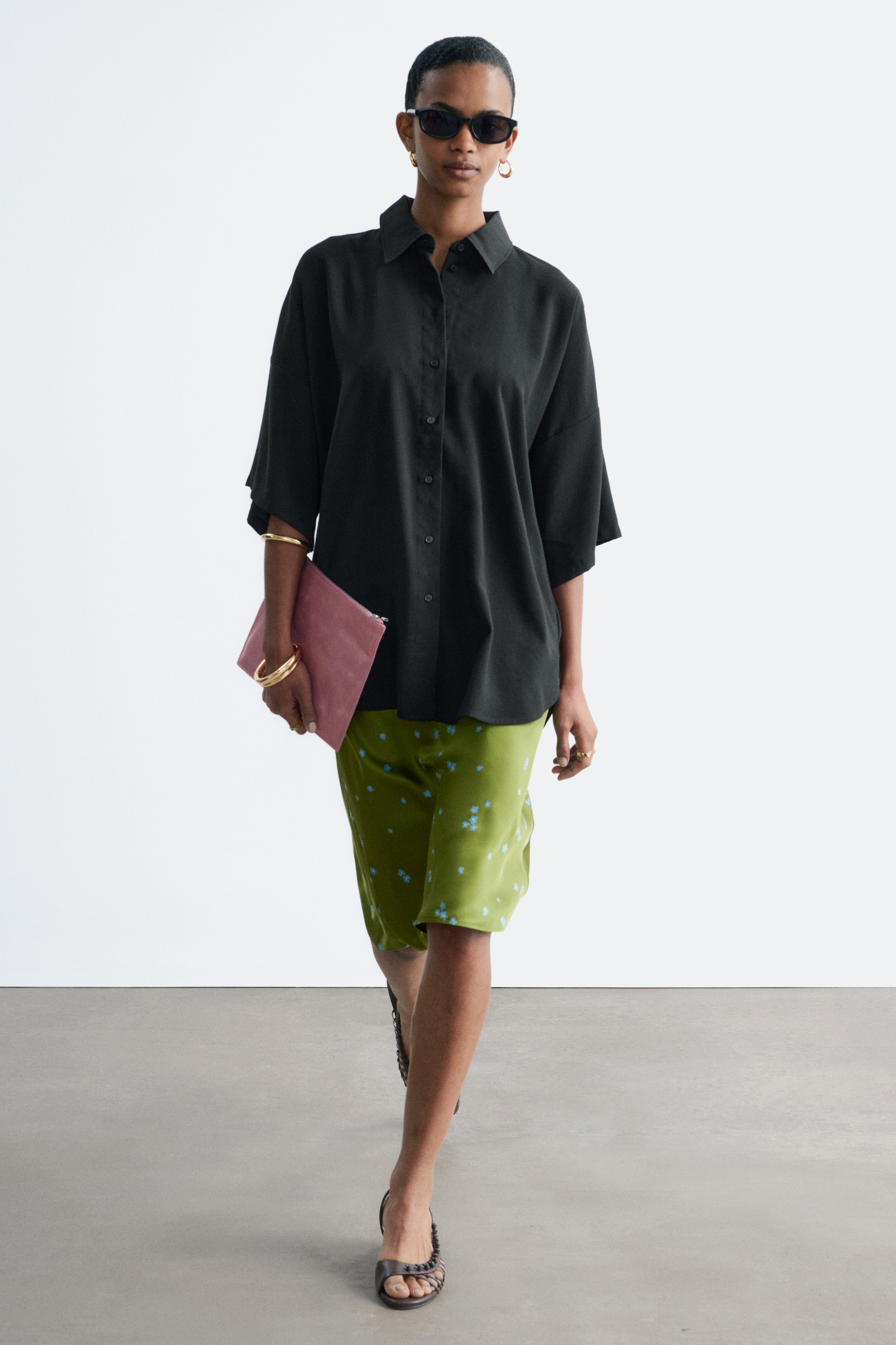 Visa större bild: En svart oversized skjorta med en lång siluett bärs av modellen. Den har en klassisk krage, knäppning fram, vida trekvartsärmar och en rundad fåll.