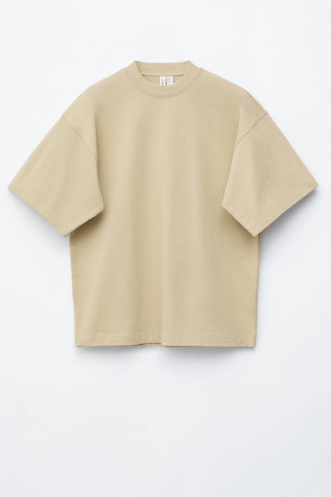 Oversize'owy t-shirt z bawełny skierowany przodem, prezentuje jasny beżowy kolor. Posiada prążkowany dekolt w stylu crew neck, opadające ramiona i szerokie krótkie rękawy, oferując luźny krój z prostym dołem. - 1