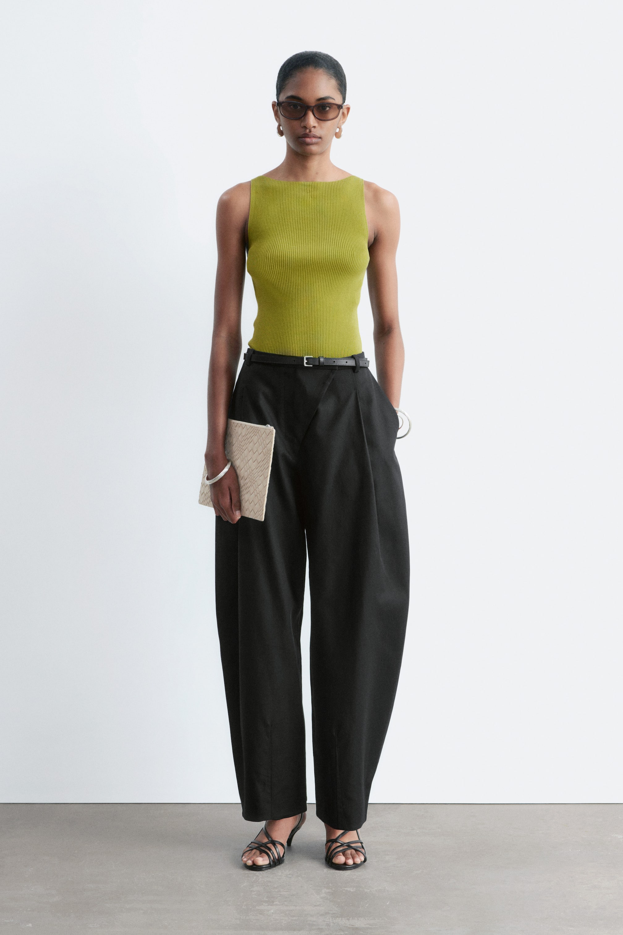 Visa större bild: Svarta vida byxor med veckad front och avslappnad passform, åtdragna i midjan med ett tunt svart bälte. Byxorna har ett flytande fall, med fållen som slutar ovanför ankeln.