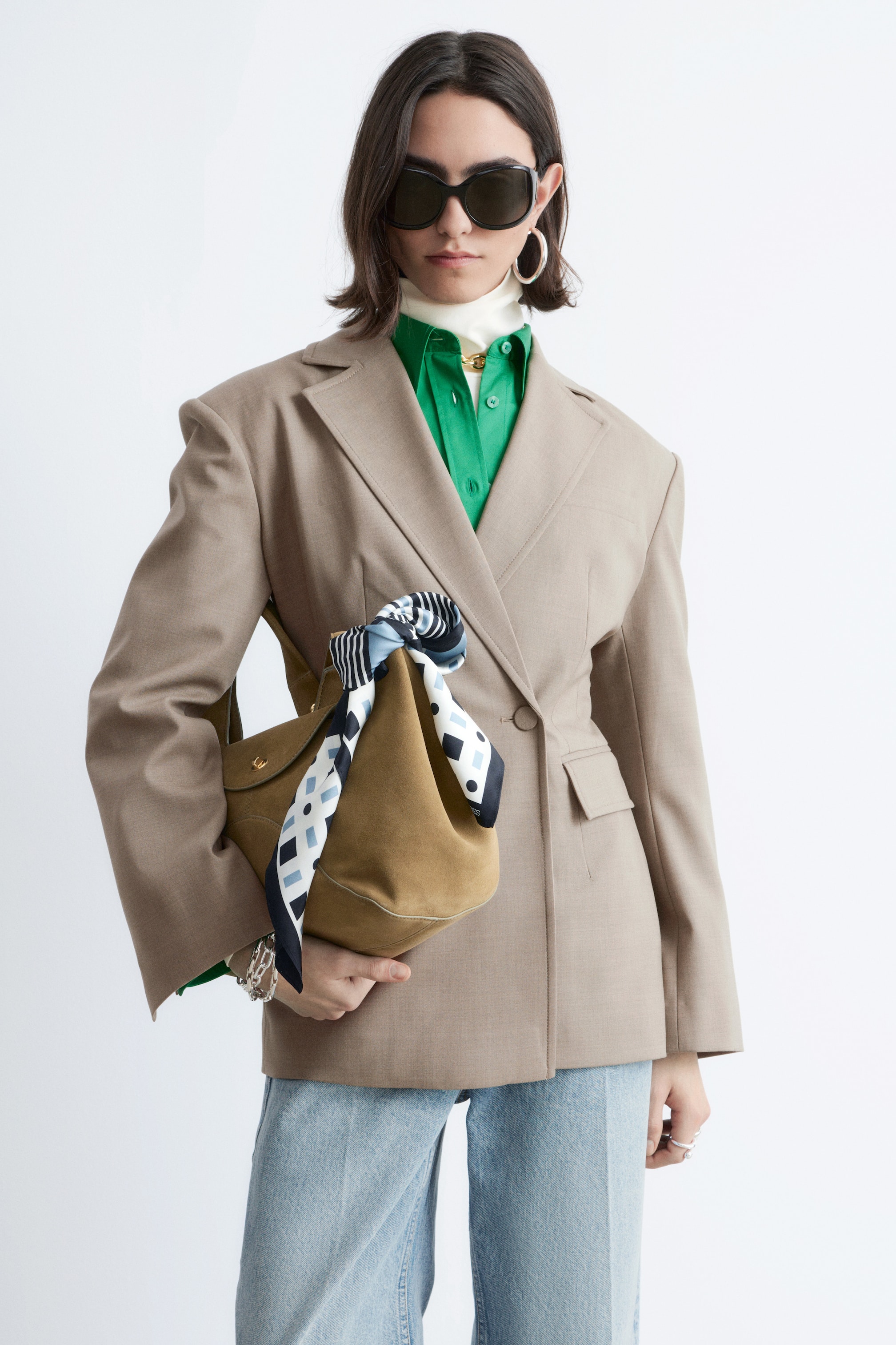 Ver imagen más grande: Se presenta una americana color topo desde un ángulo frontal izquierdo ligeramente inclinado, con solapas de muesca, hombros estructurados y cierre de dos botones con uno abrochado. Muestra un ajuste entallado con bolsillos de solapa en el frente y está superpuesta sobre una camisa verde con cuello y un jersey de cuello alto blanco.