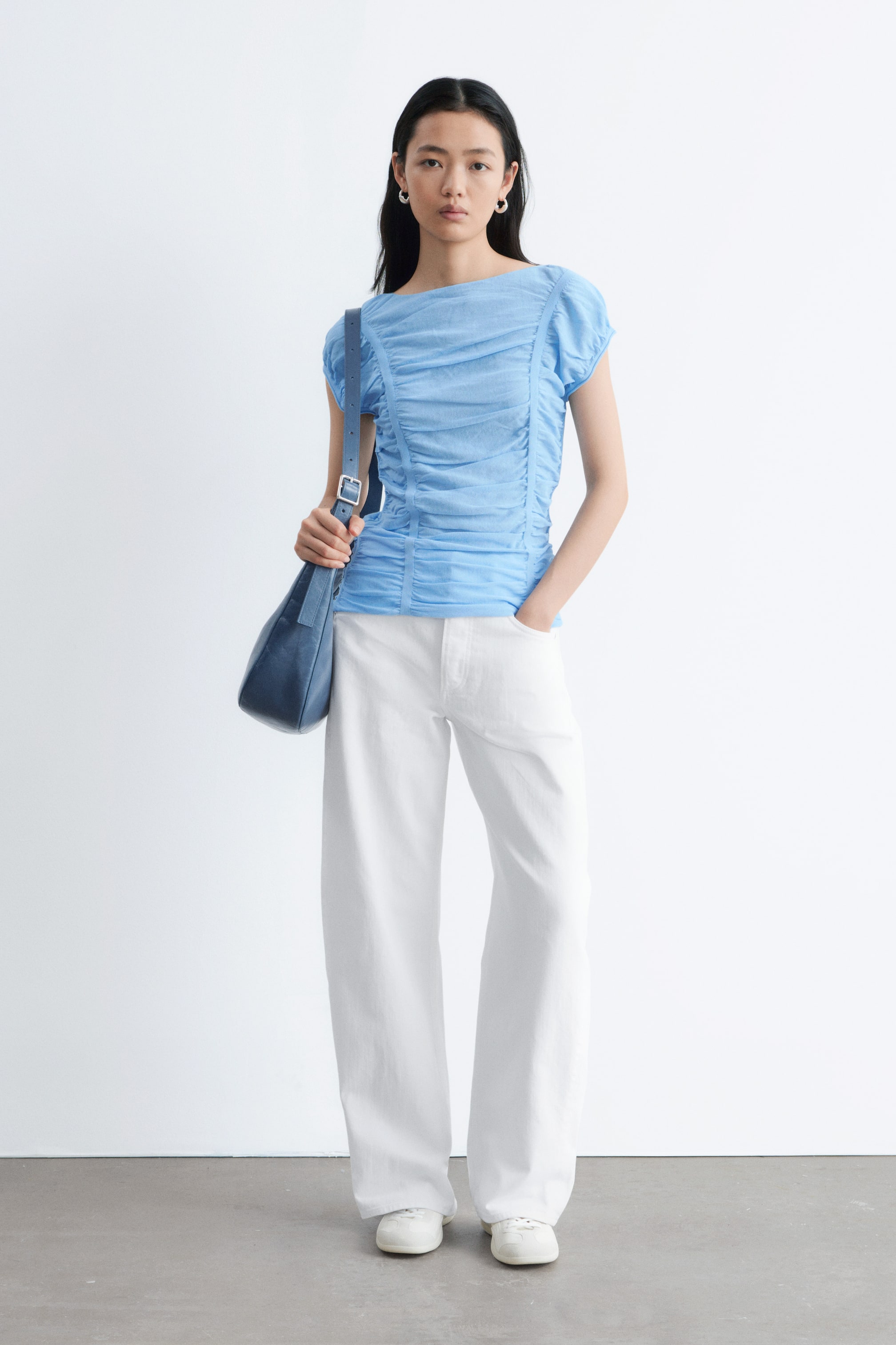 Ver imagen más grande: La blusa fruncida de color azul claro se presenta desde el frente, con un amplio escote barco y mangas cortas recogidas. El fruncido extenso a lo largo del cuerpo crea una silueta texturizada y ajustada.