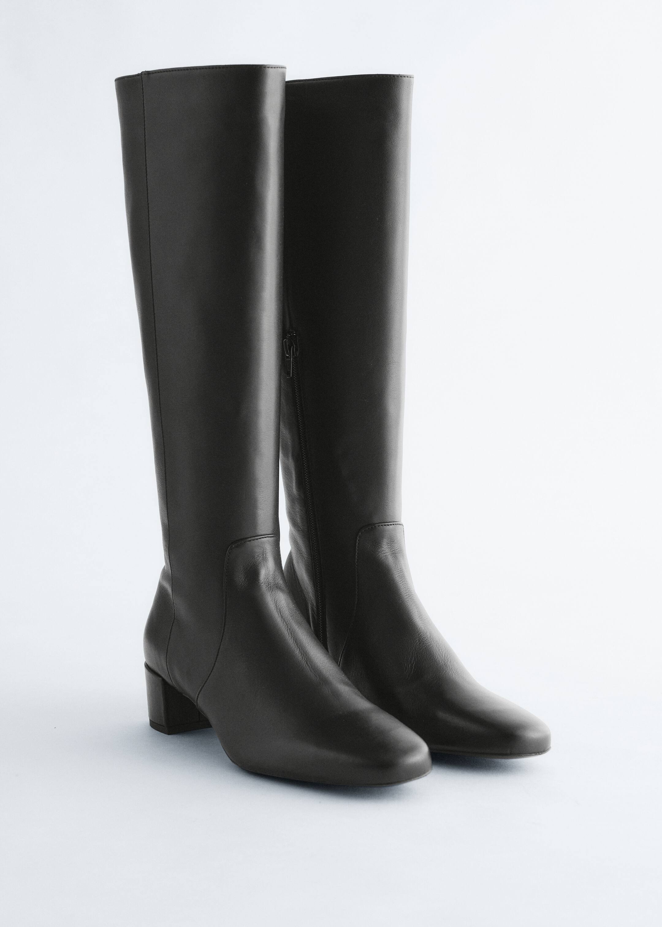 Ver imagem maior: Duas botas de cano alto em couro preto estão de pé, com canos ajustados, bicos em amêndoa e saltos em bloco. Um fecho de correr lateral é visível no lado interno de uma das botas.