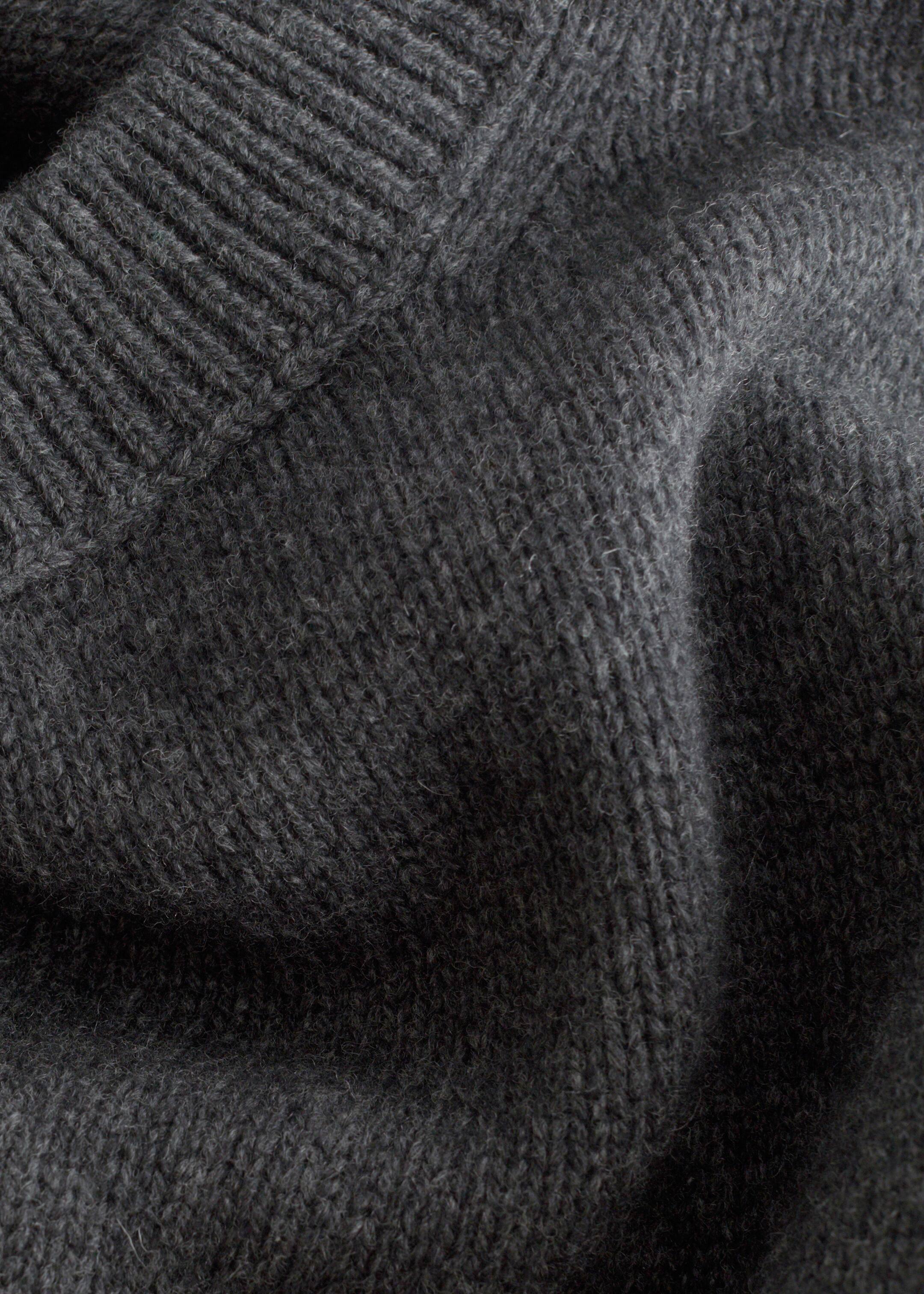 Größeres Bild ansehen: Der dunkelgraue Strickstoff eines Pullovers zeigt eine weiche, leicht flauschige Textur, mit einem sichtbaren gerippten Strickbesatz, der diagonal über die obere linke Seite verläuft.