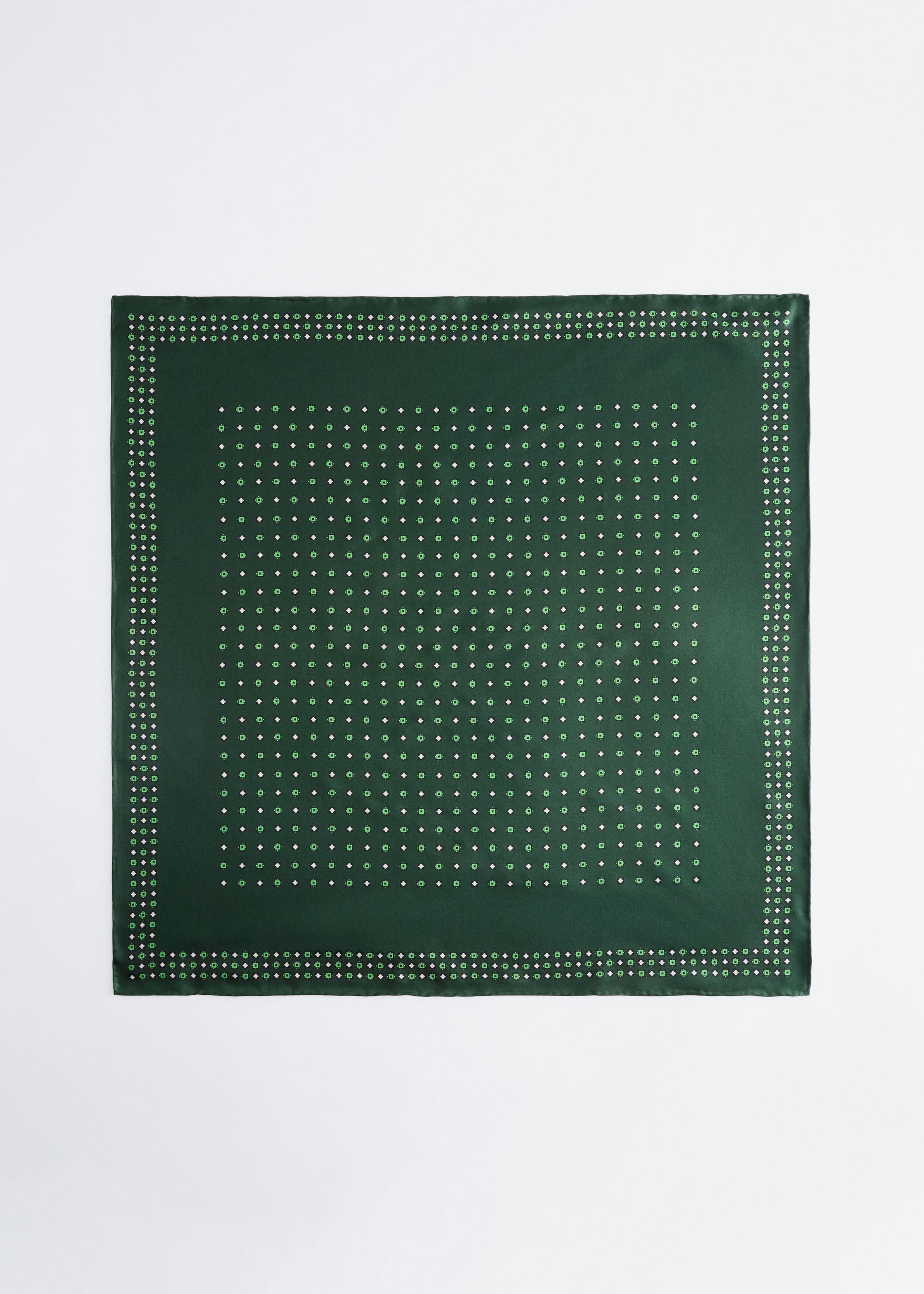 A square dark green pocket square is lying flat and facing forward, displaying a repeating grid pattern of tiny white and light green geometric motifs. The design features a matching patterned inner border and a solid dark green stitched edge.
