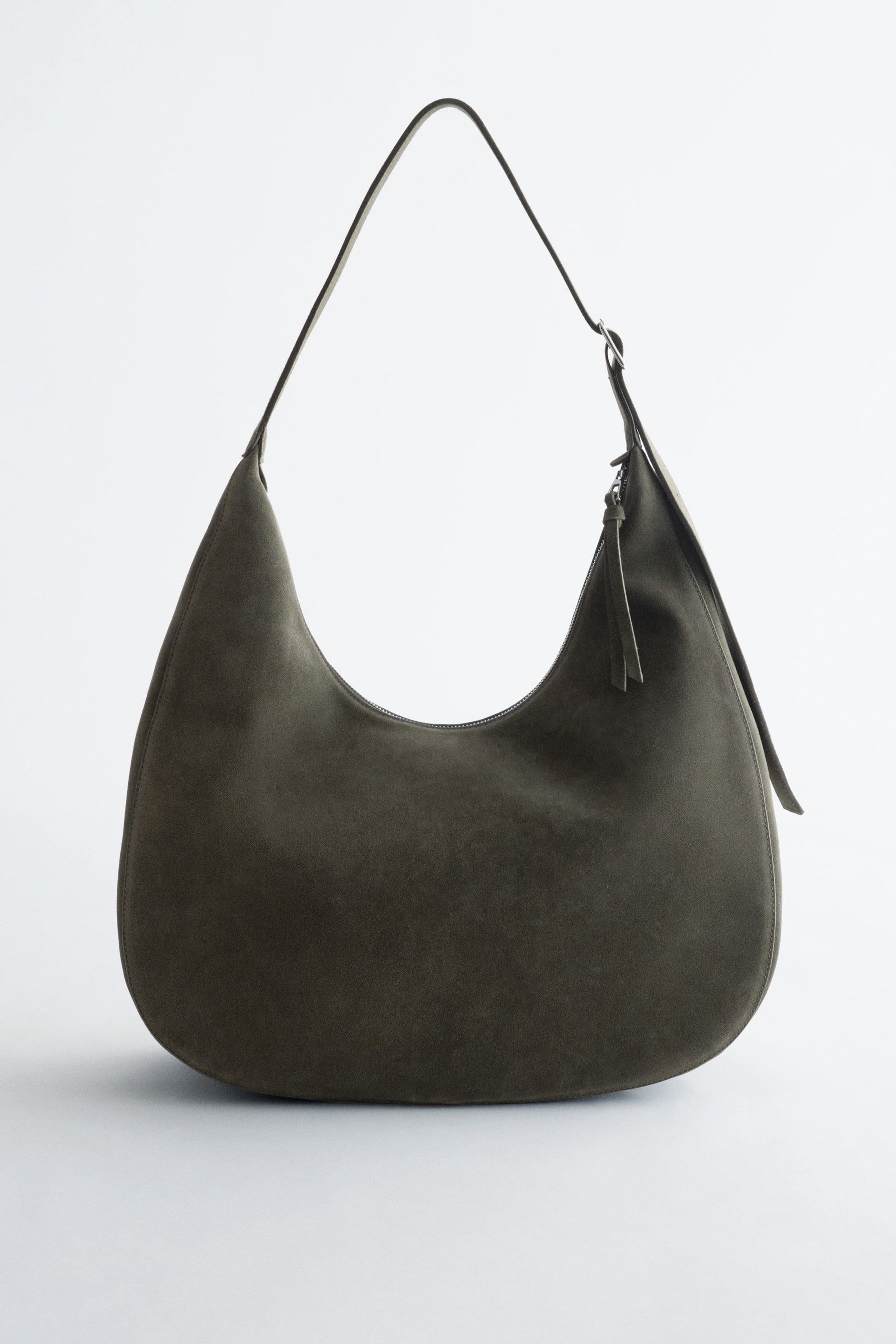 View larger image: A dark olive suede shoulder bag is presented from the front, showcasing a rounded, crescent-shaped silhouette. It features a single, thin shoulder strap and a top zip fastening with a small pull tab.