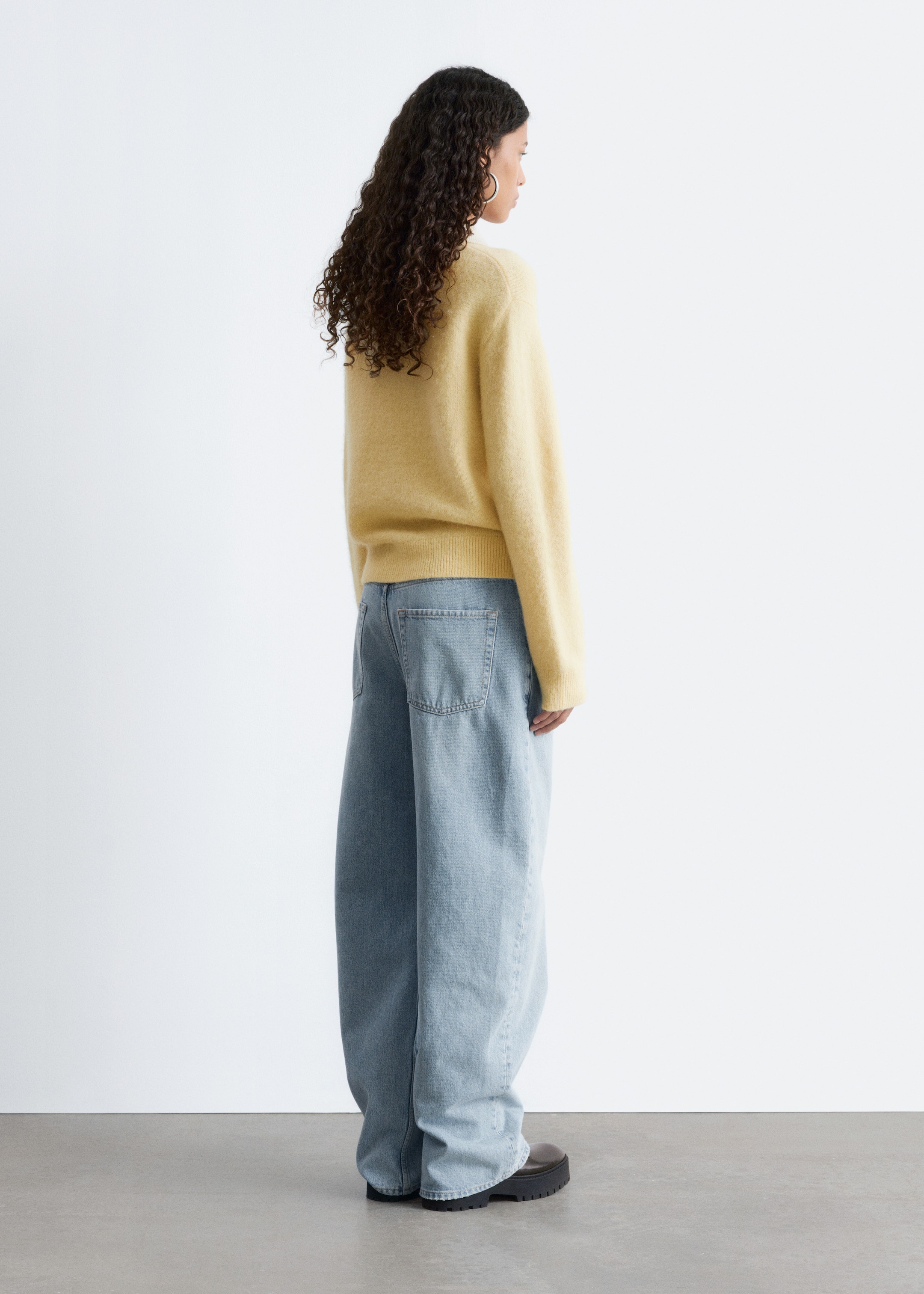 View larger image: A light yellow fuzzy sweater with long sleeves and a ribbed hem is being worn, styled with light blue wide-leg jeans showing visible back pockets. Dark shoes with chunky soles are also being worn, all viewed from the back and side.