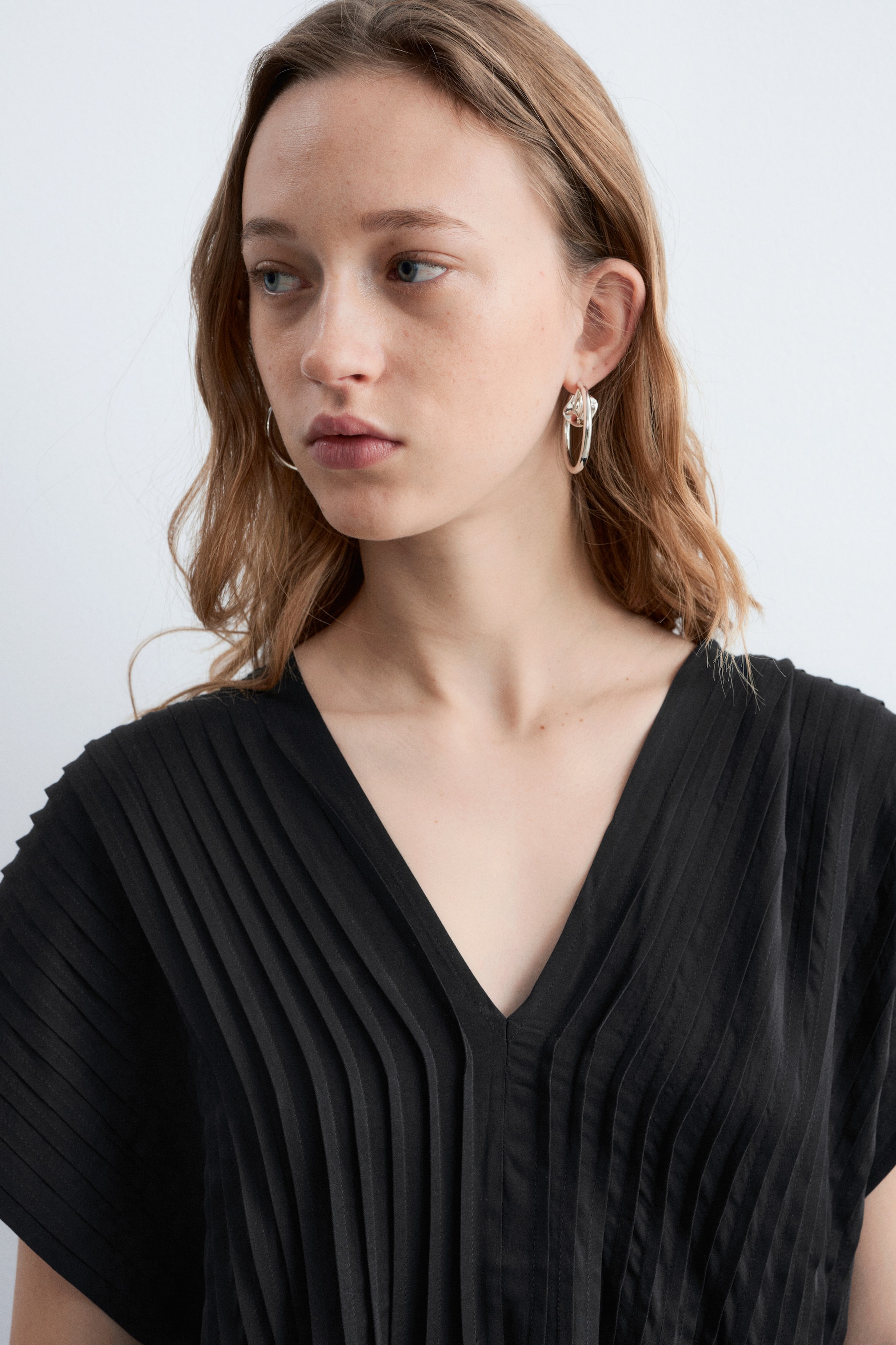 Agrandir l'image: Une boucle d'oreille en anneau de couleur argentée est portée à l'oreille, présentant un grand anneau extérieur avec un élément plus petit, en forme de nœud torsadé, suspendu à l'intérieur.